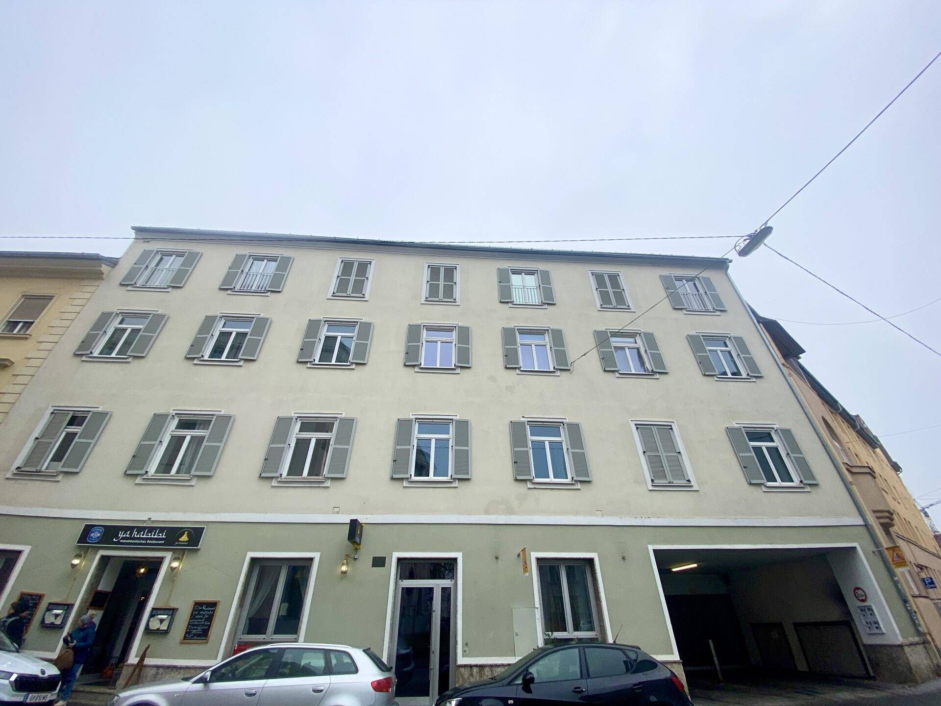 Klassisches Mehrfamilienhaus mit vielen Fenstern und Fensterläden in einer städtischen Umgebung.