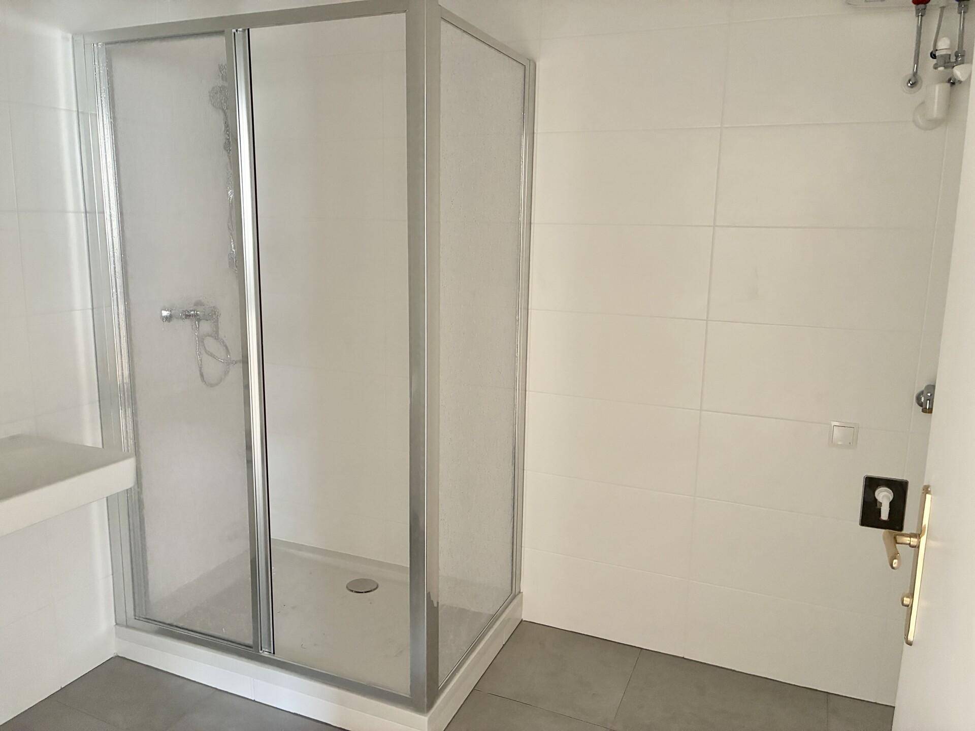 Modernes Badezimmer mit weiß gefliesten Wänden, grauen Bodenfliesen und einer Duschkabine.
