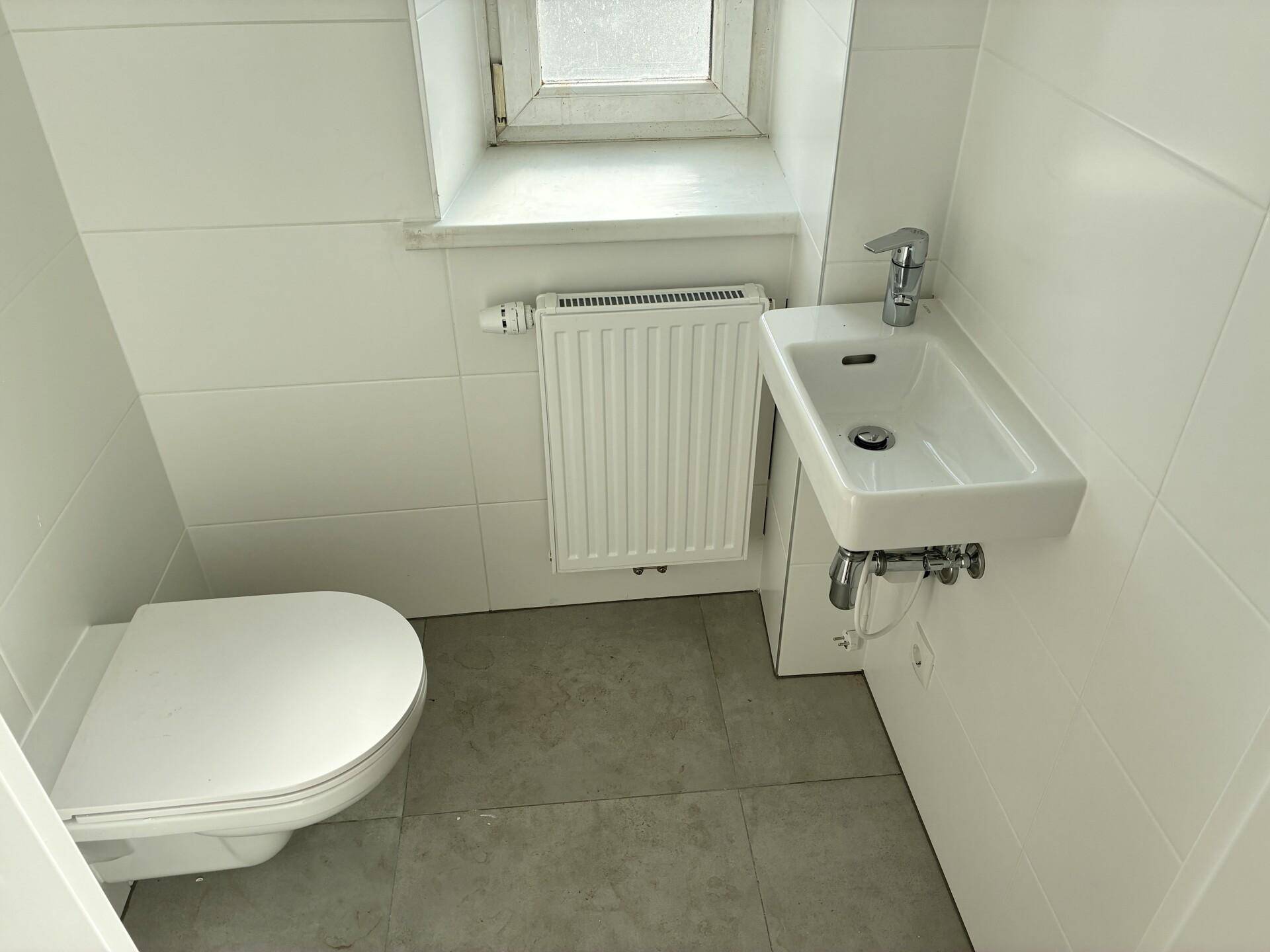 Kleines Gäste-WC mit Fenster, wandhängendem WC und einem kompakten Waschbecken.