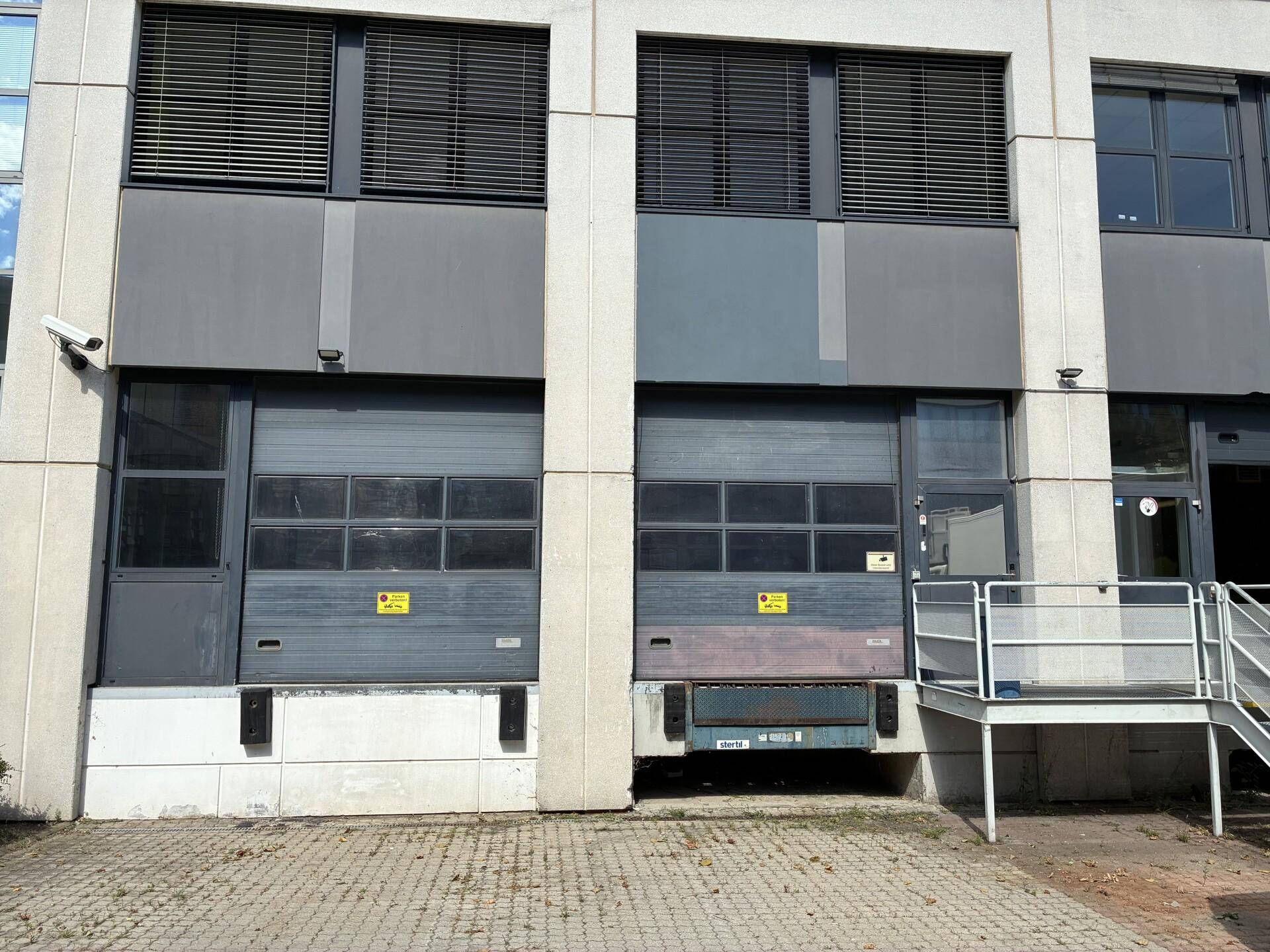 Detailansicht der Laderampen und des Eingangsbereichs eines Gewerbegebäudes mit Rolltoren und Treppe.