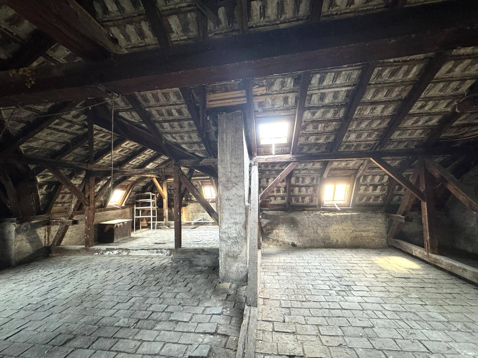 Geräumiger Dachboden mit sichtbaren Holzbalken, Ziegeldach und kleinen Dachfenstern, ideal für einen Ausbau.