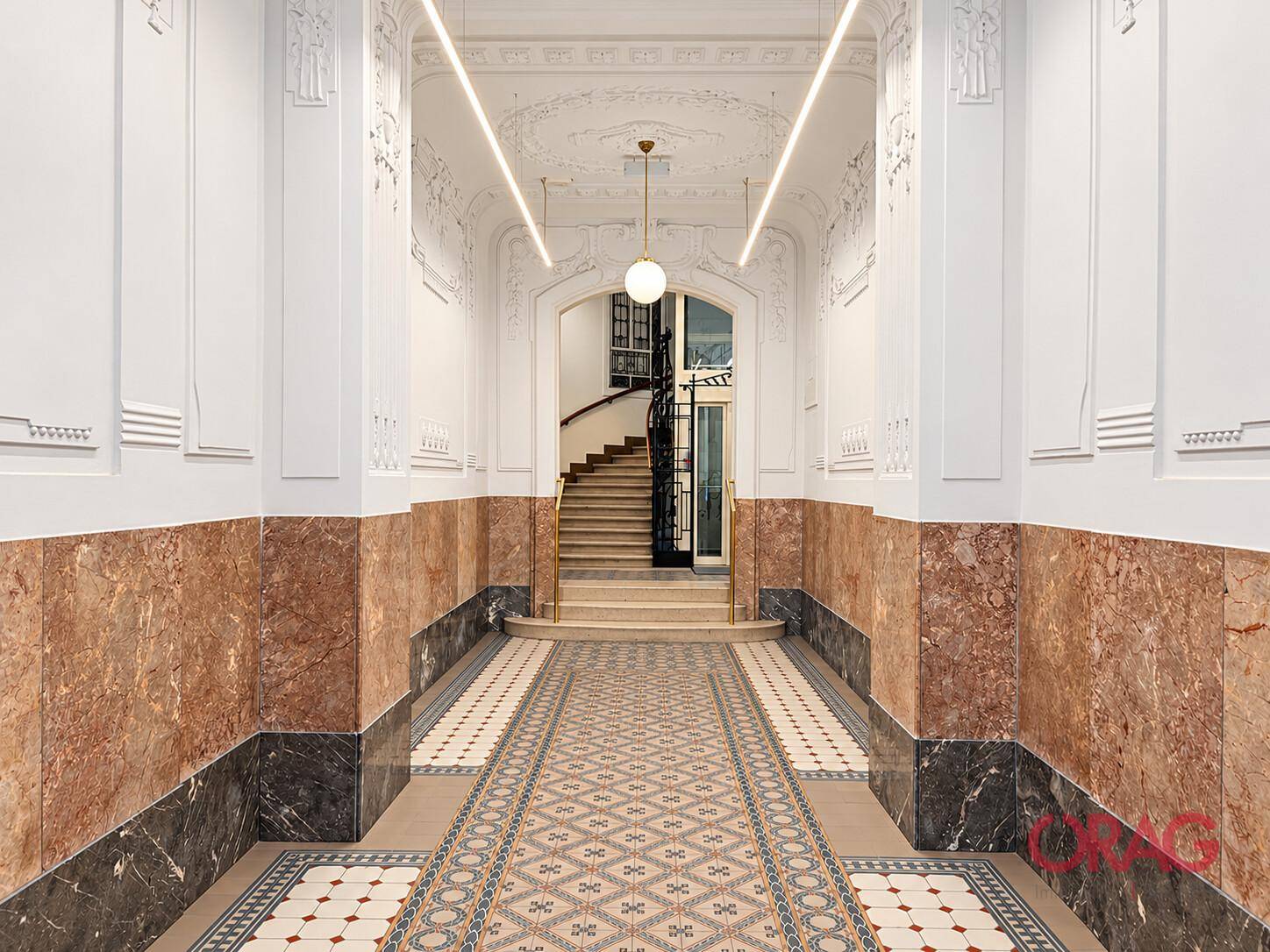 Prächtiger Eingangsbereich mit Marmorverkleidung, gemusterten Fliesen und einer geschwungenen Treppe im Hintergrund.