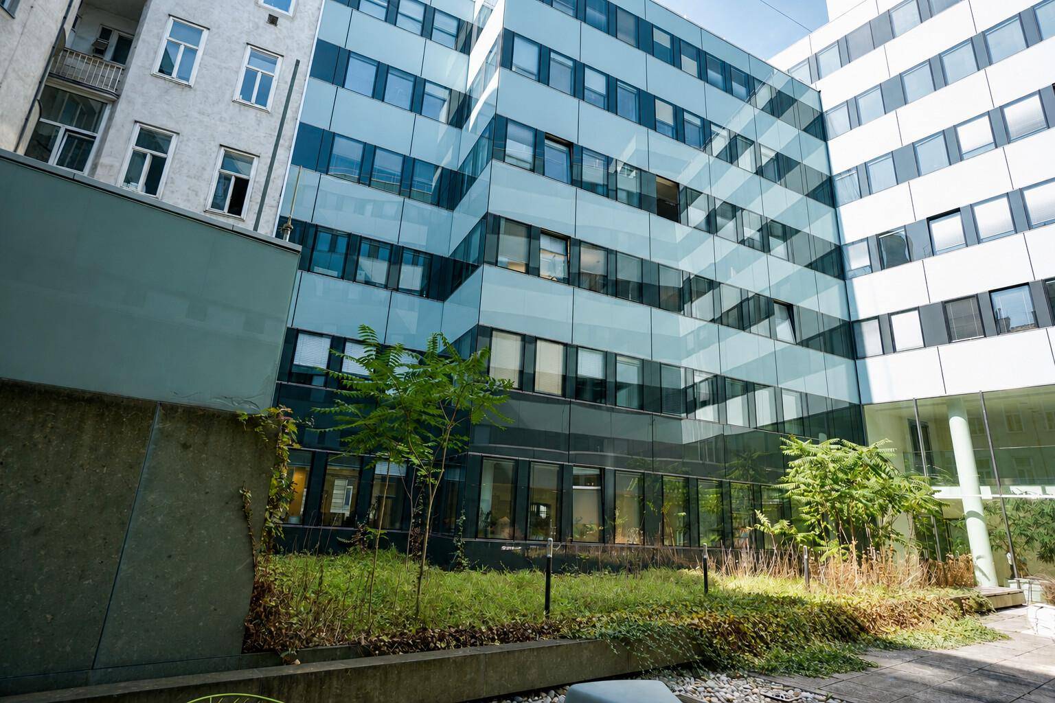Moderner Gebäudekomplex mit begrüntem Innenhof und Glasfassaden, die eine zeitgemäße Architektur zeigen.