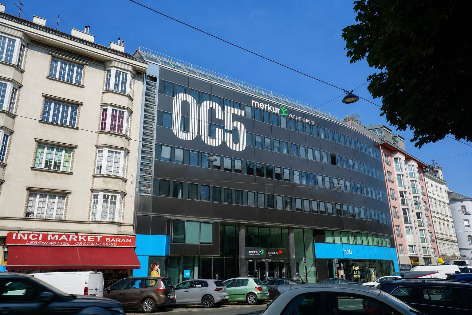 Moderne Bürogebäude-Fassade mit großen Fenstern und Firmenbeschriftung an einer belebten Stadtstraße.