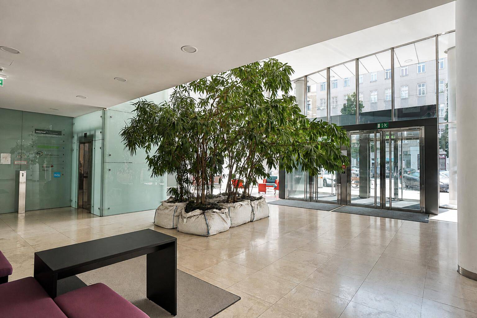 Geräumige und helle Lobby mit großer Glasfassade, Drehtür, Aufzug und einer beeindruckenden Pflanzeninstallation.