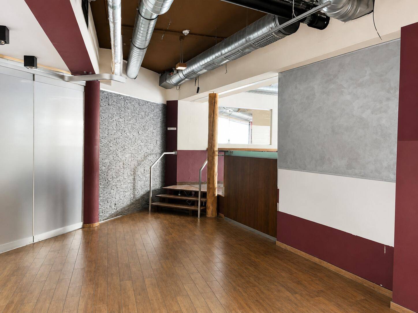 Offener Gewerberaum mit Holzboden, freiliegenden Rohren, einer kleinen Treppe und strukturierten Wänden.