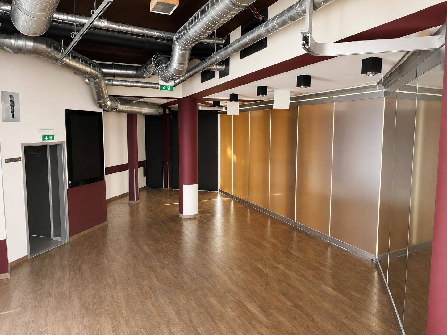 Heller Gewerberaum mit Holzboden, freiliegenden Rohren, modernen Wandverkleidungen und einem Aufzug.