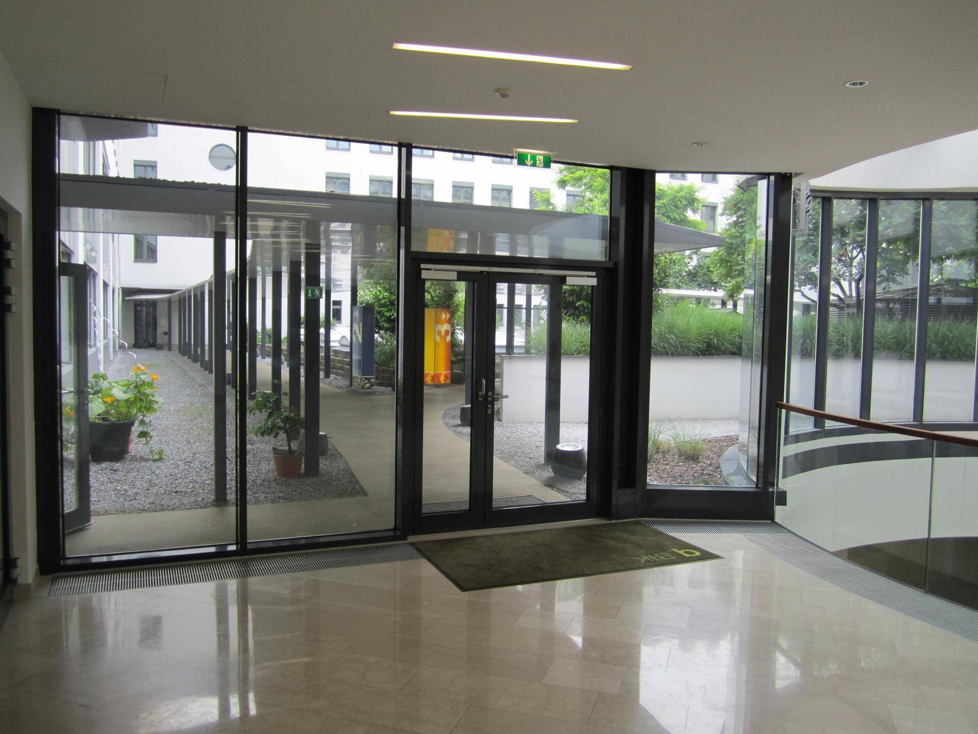 Heller Eingangsbereich mit großen Glasfronten, die den Blick auf den begrünten Innenhof freigeben.