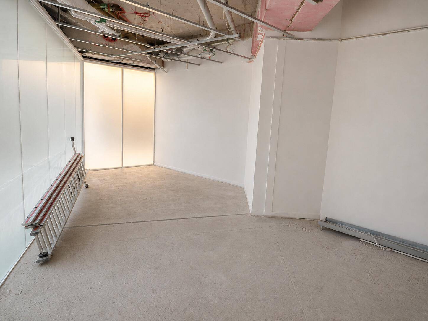 Unfertiger Büroraum mit Betonboden, weißen Wänden und einer großen, mattierten Fensterfront, bereit zum Ausbau.