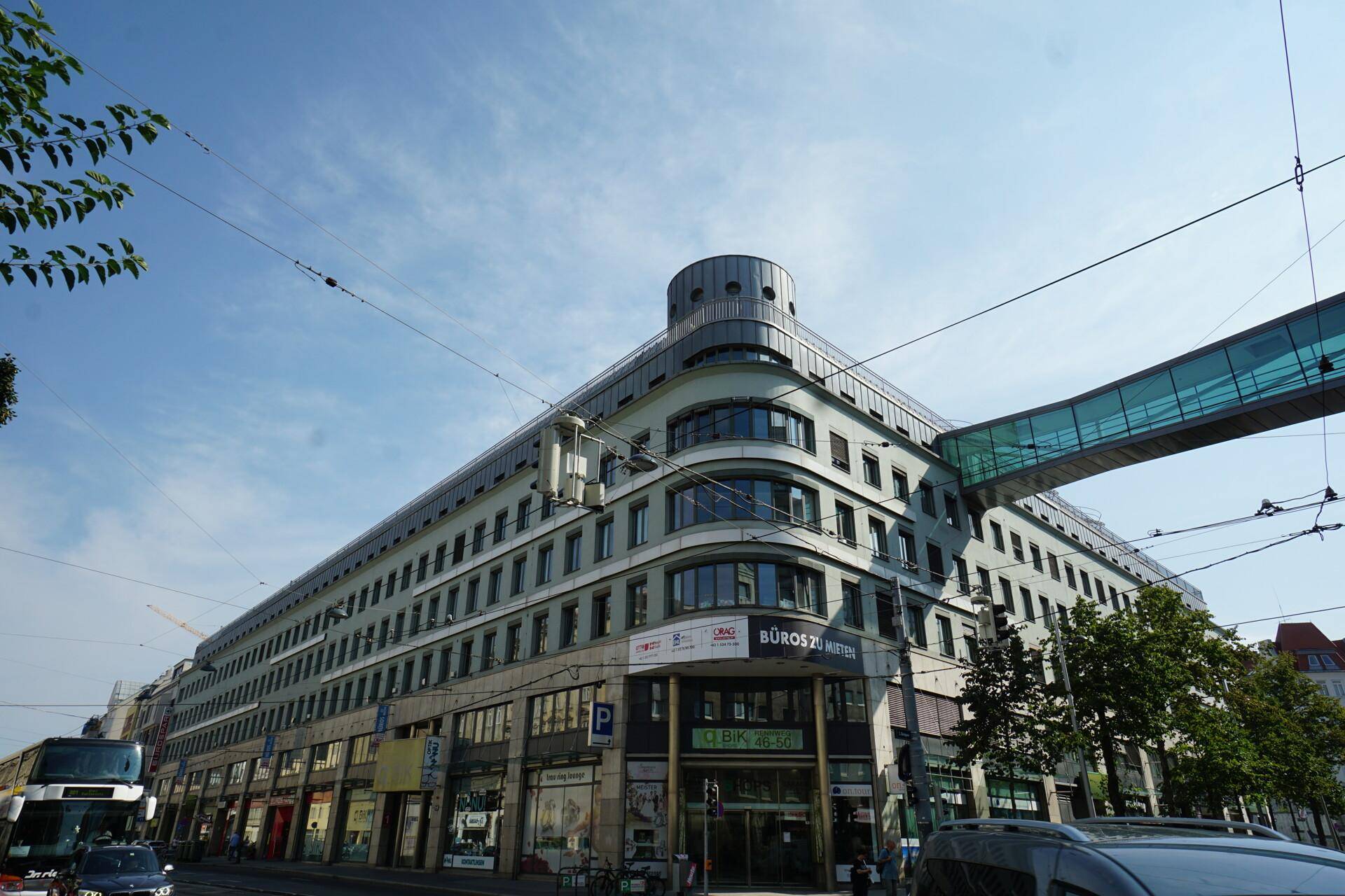 Großes Geschäftsgebäude mit moderner Architektur, vielen Fenstern und einer Fußgängerbrücke in der Stadt.