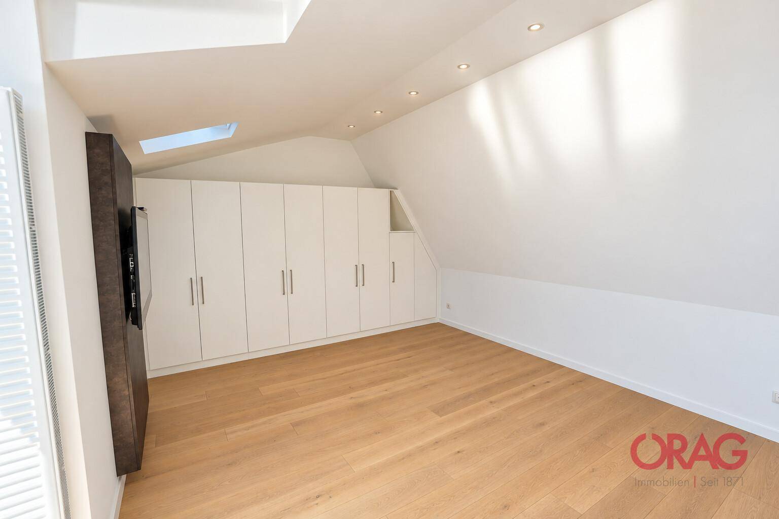 Helles Schlafzimmer mit Dachschrägen, Einbauschränken und einem Dachfenster, das natürliches Licht spendet.