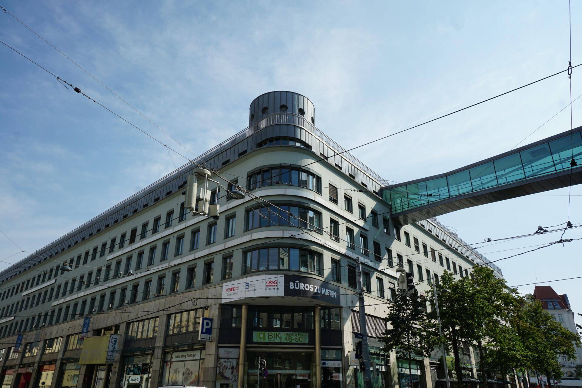 Großes Bürogebäude mit moderner Architektur, runder Ecke und einer Fußgängerbrücke über die Straße.