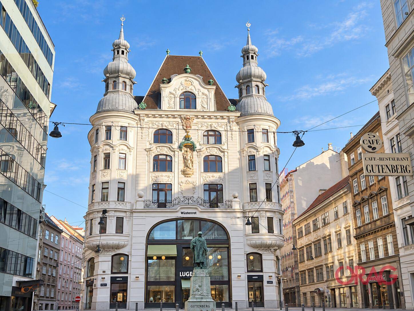 Prachtvolles historisches Gebäude mit Türmchen und Statuen, umgeben von weiteren Gebäuden und einem Café.