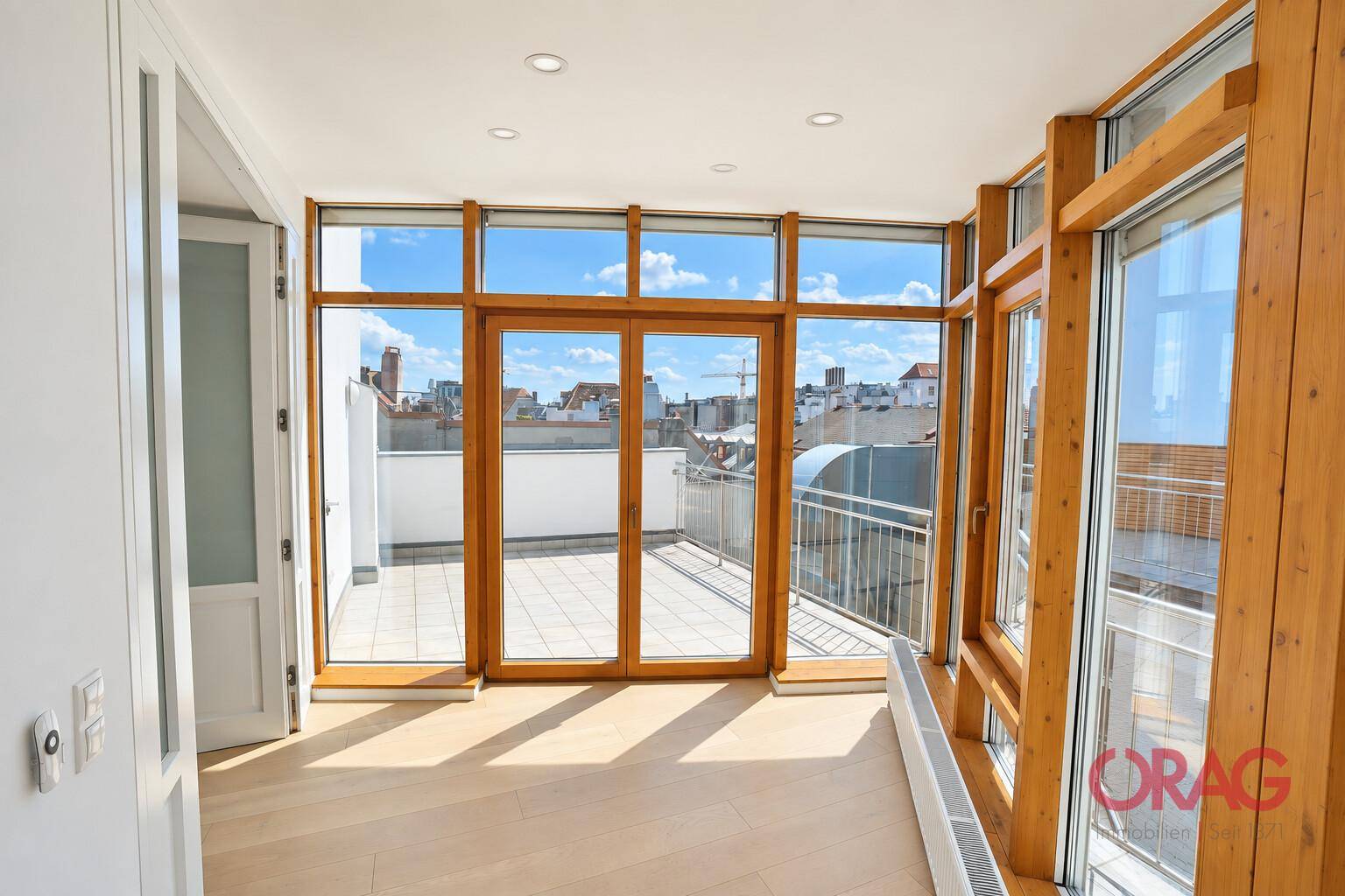 Heller Wohnraum mit großen Holzfenstern, Zugang zu einer Terrasse und weitem Blick über die Stadt.