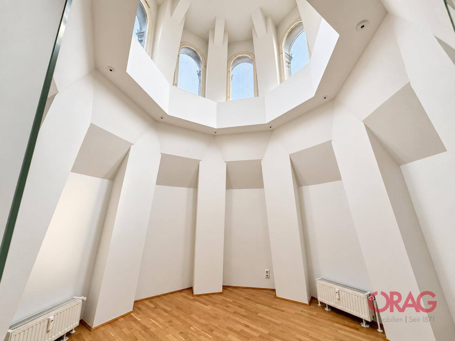 Einzigartiger Raum mit hoher, gewölbter Decke, mehreren Bogenfenstern und hellem Holzfußboden.