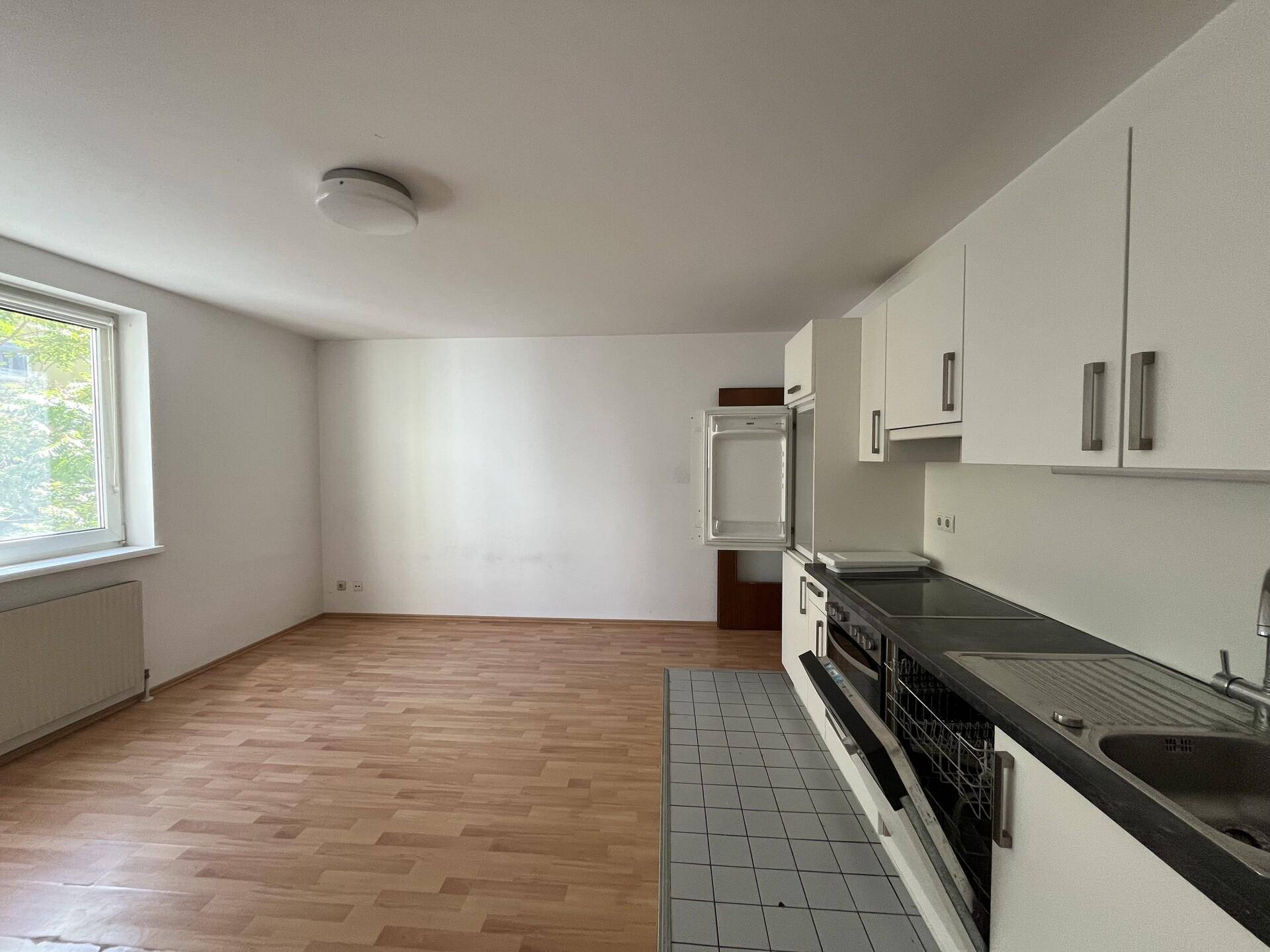Heller Wohnbereich mit integrierter Küchenzeile, Laminatboden und großem Fenster für viel Tageslicht.
