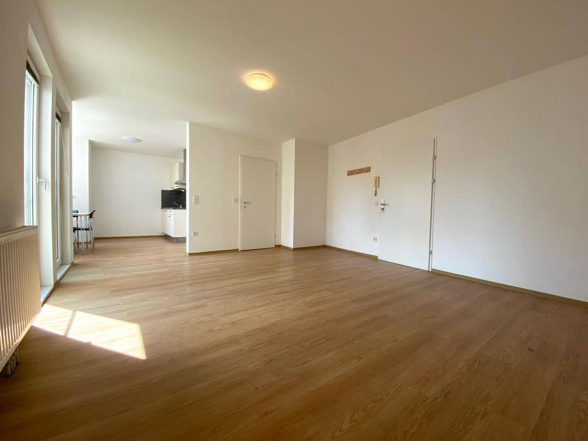 Geräumiges Wohnzimmer mit Laminatboden und offenem Übergang zum Küchenbereich.