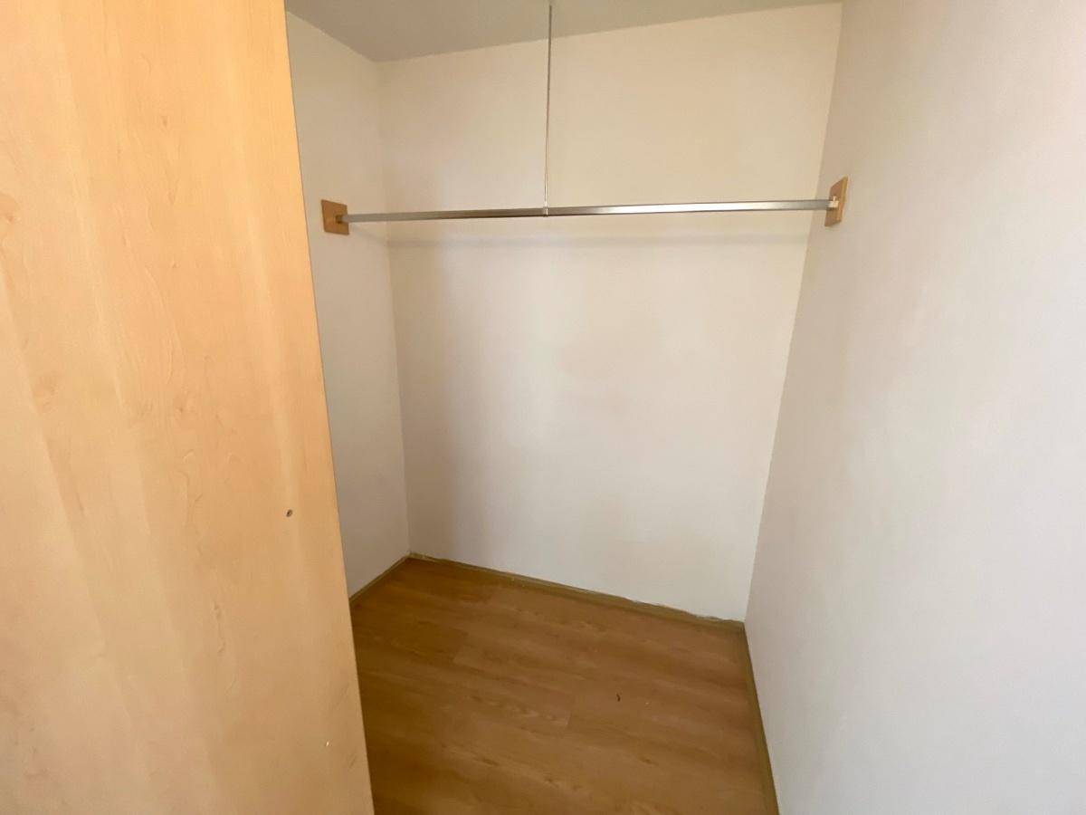 Kleiner Raum mit Kleiderstange und Laminatboden, nutzbar als Abstellraum oder begehbarer Kleiderschrank.