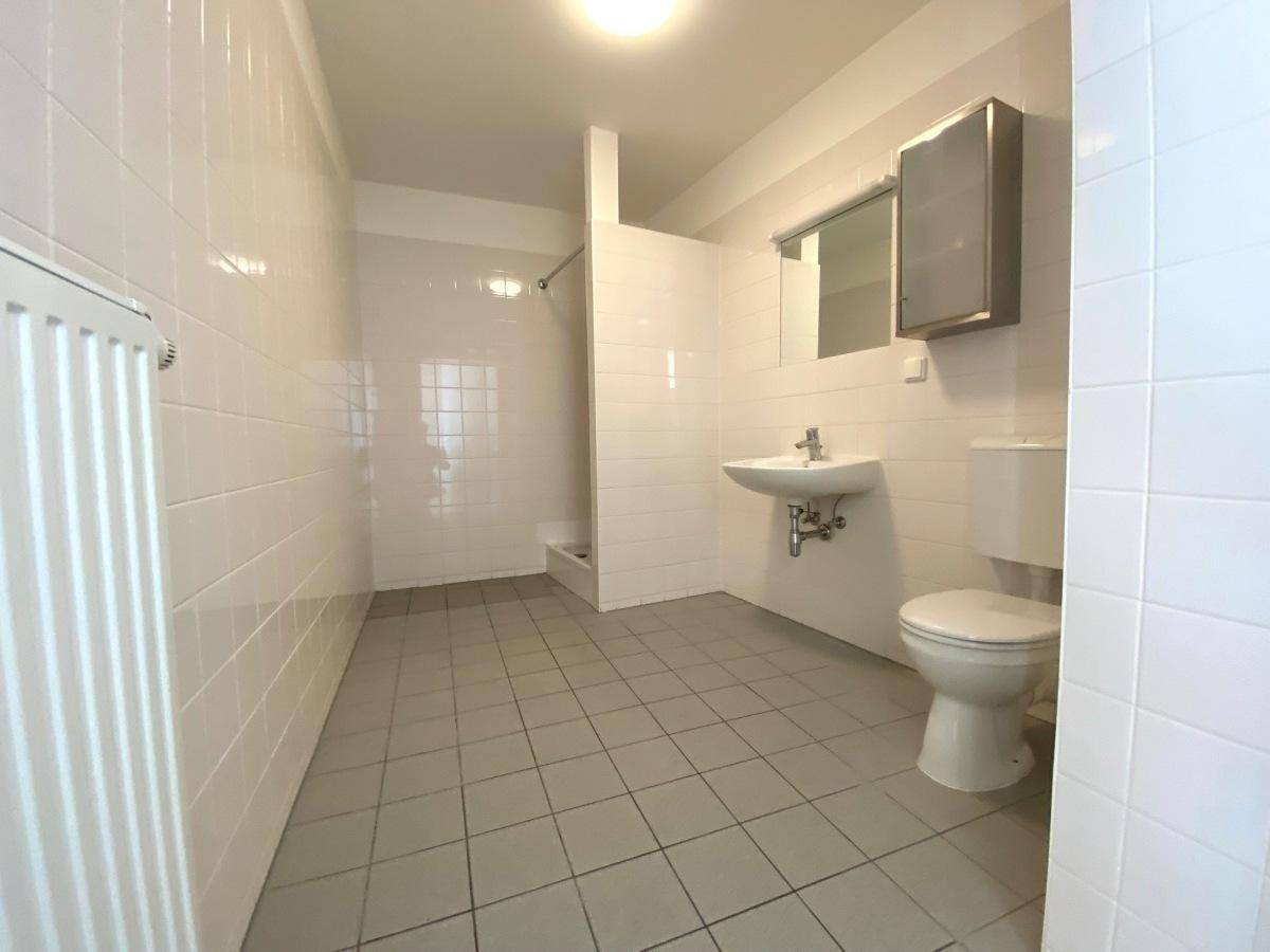 Funktionales Badezimmer mit Dusche, WC, Waschbecken und weißen Fliesen an Wänden und Boden.