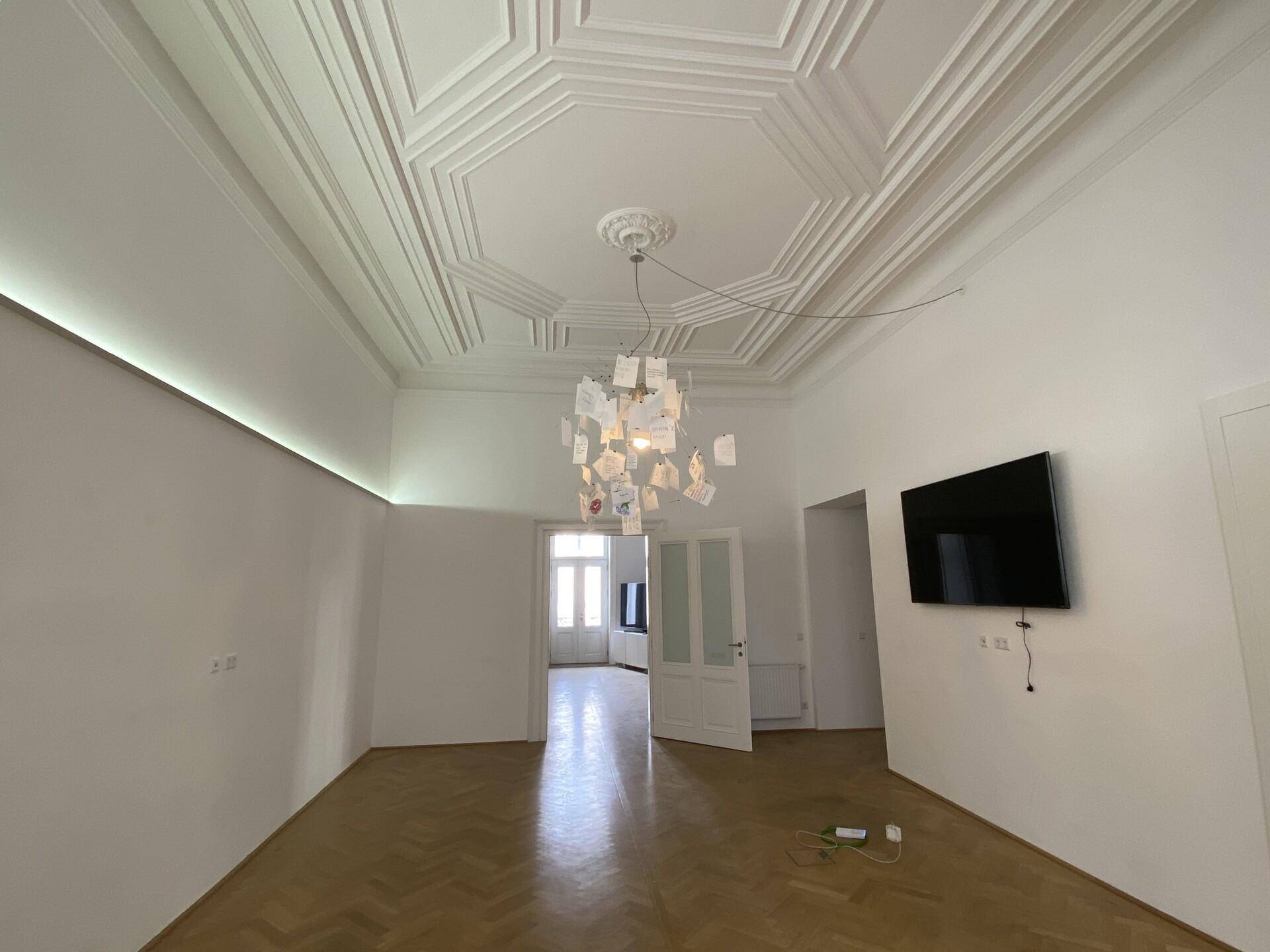 Heller Wohnraum mit Fischgrätparkett, Stuckdecke und einer modernen Designerlampe als Blickfang.