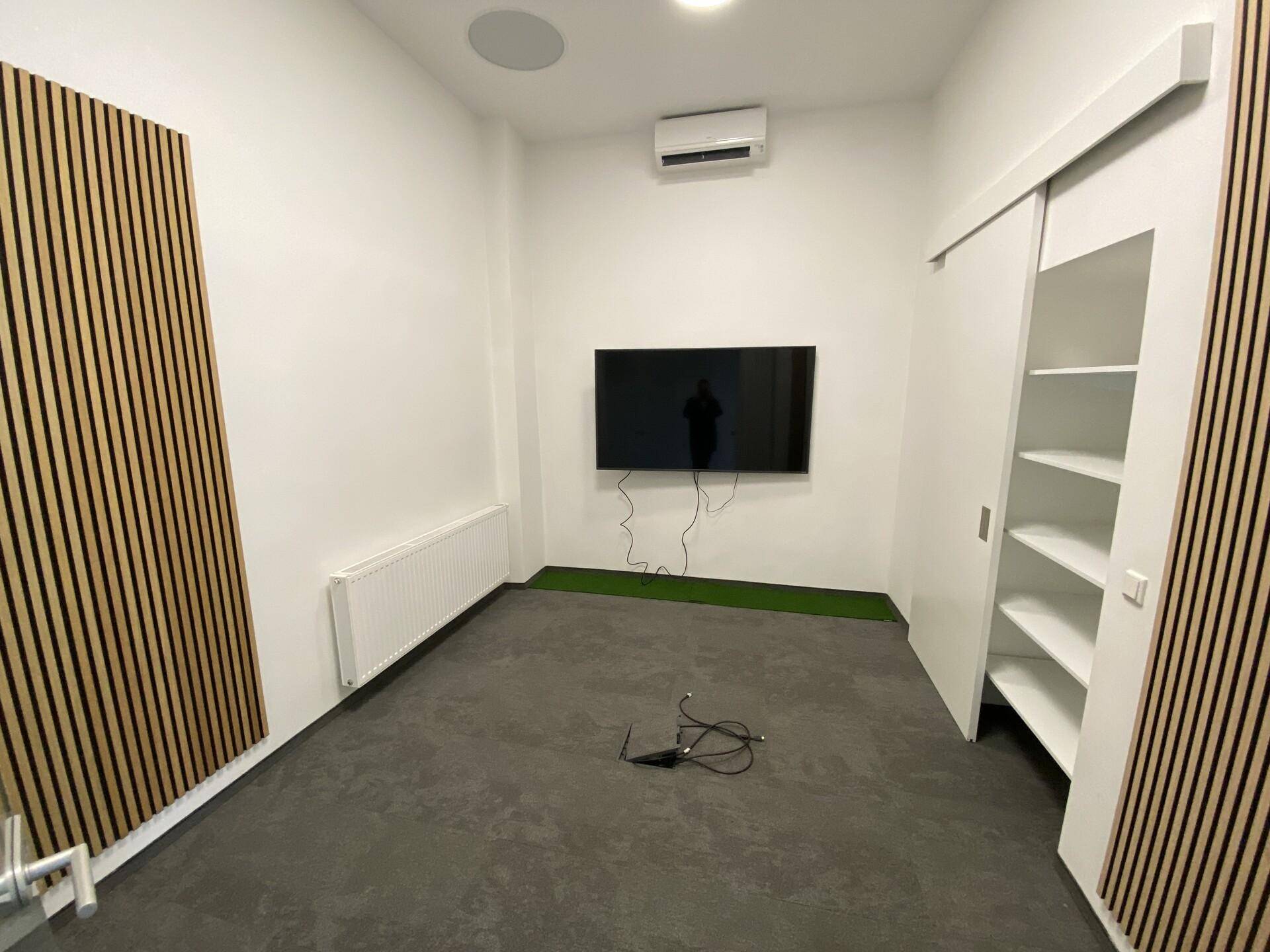 Kleiner Büroraum mit Akustikpaneelen, Klimaanlage und einem Wandfernseher.
