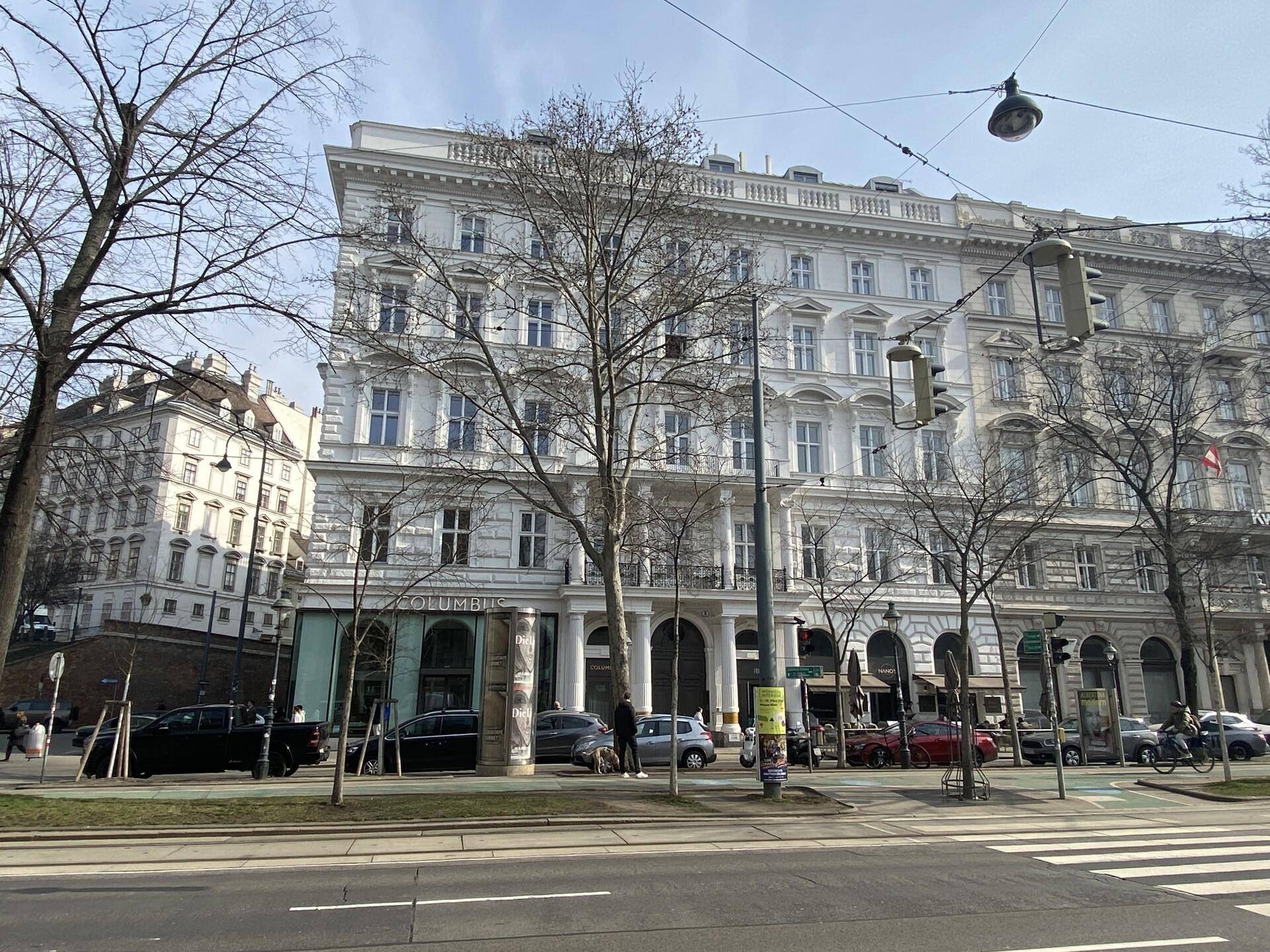 Historisches Gebäude mit klassischer Architektur, vielen Fenstern und Geschäften im Erdgeschoss.