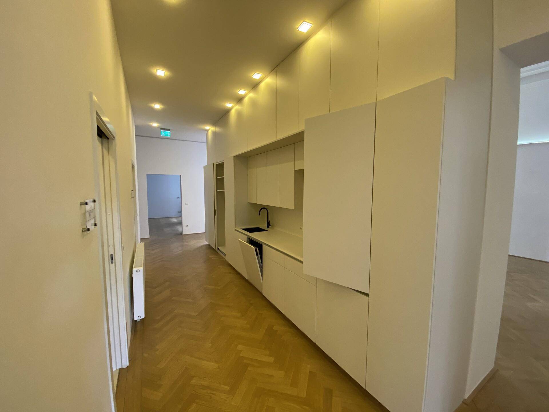 Langer Flur mit integrierter Küchenzeile, Fischgrätparkett und moderner Deckenbeleuchtung.