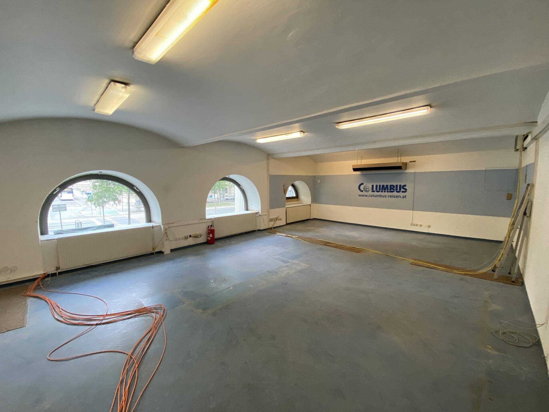 Leerer Büroraum mit gewölbter Decke, Bogenfenstern und Kabelinstallationen.
