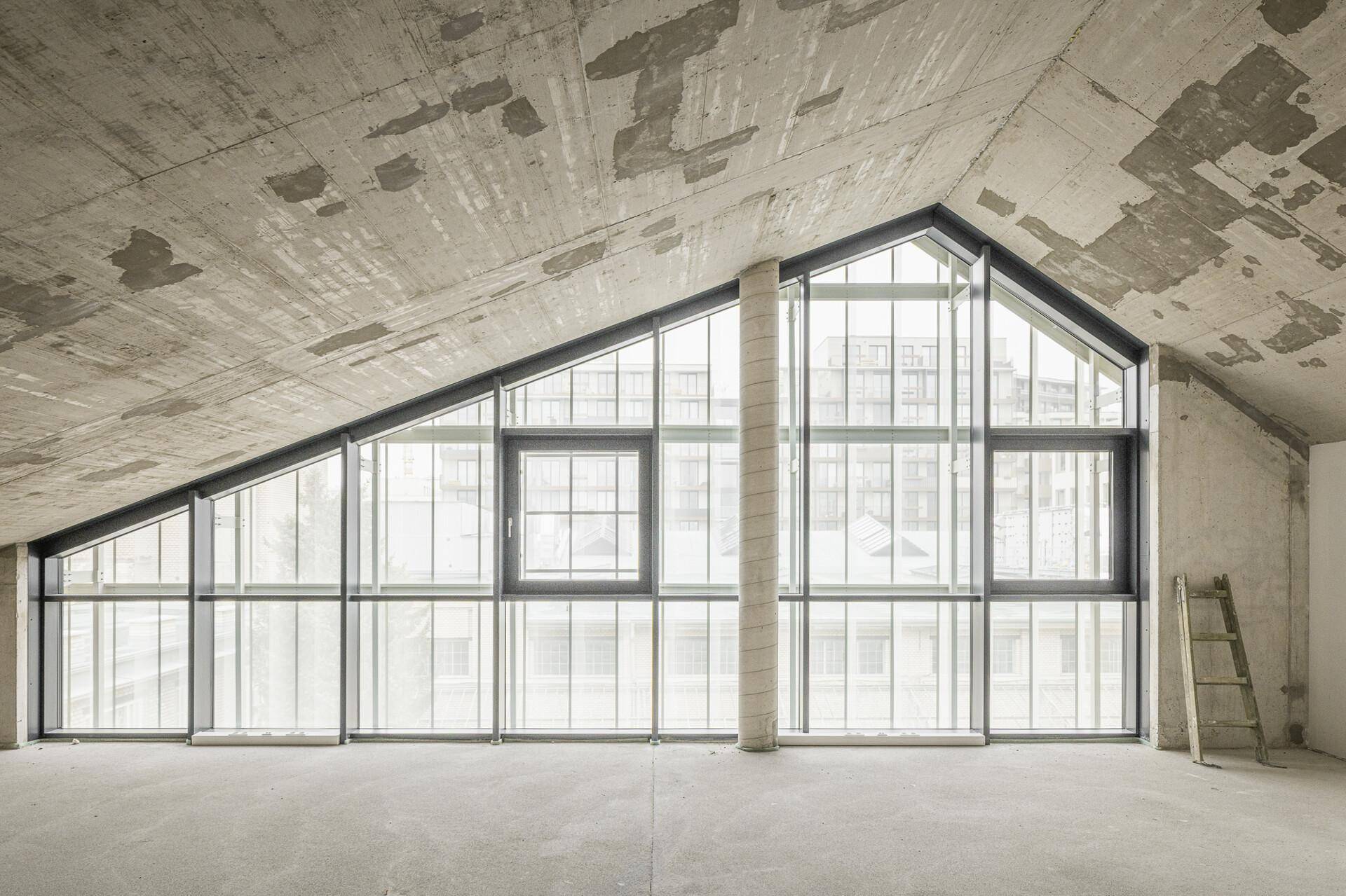 Großer Raum mit schräger Betondecke und beeindruckender, dreieckiger Glasfassade, noch im Rohbau.