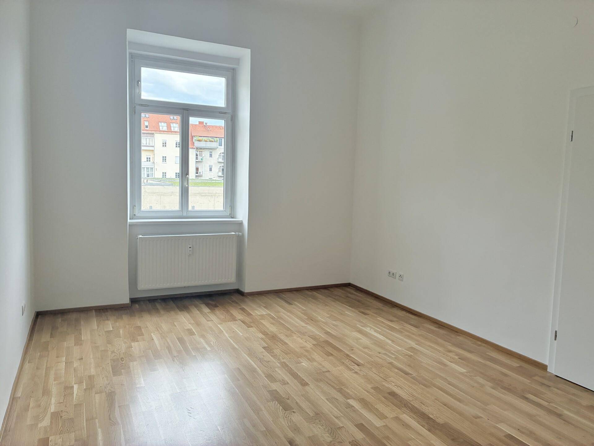 Geräumiger, heller Raum mit Parkettboden und Blick auf die gegenüberliegenden Gebäude.