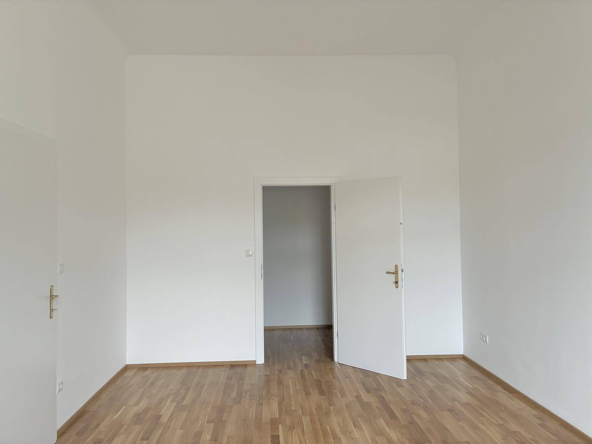 Leerer Raum mit Parkettboden und weiß gestrichenen Wänden, bereit zur individuellen Gestaltung.