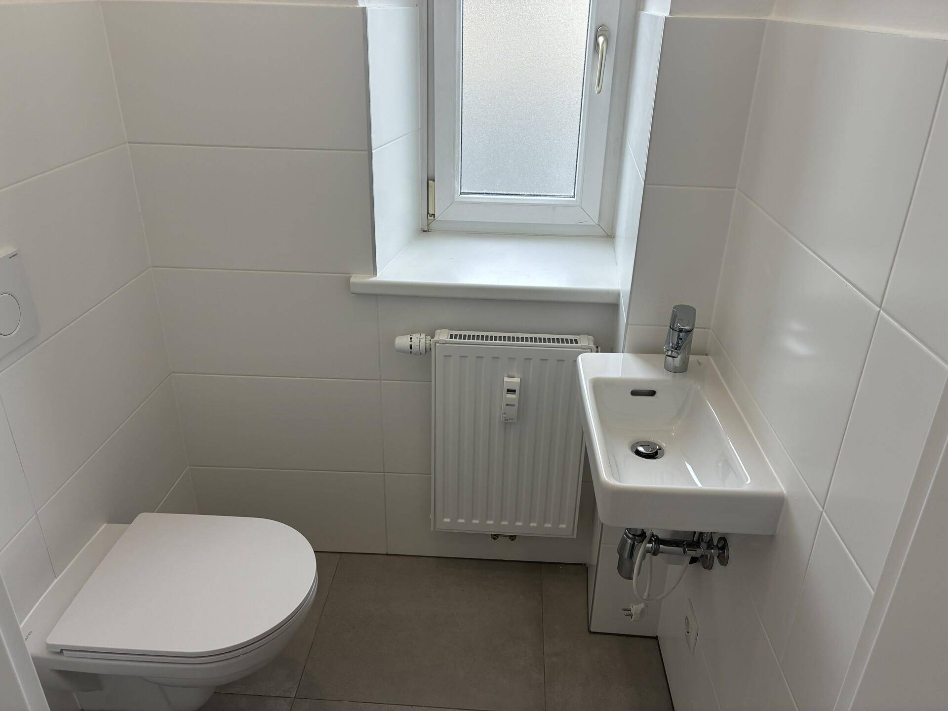 Helles Gäste-WC mit Fenster, wandhängender Toilette und kleinem Waschbecken.