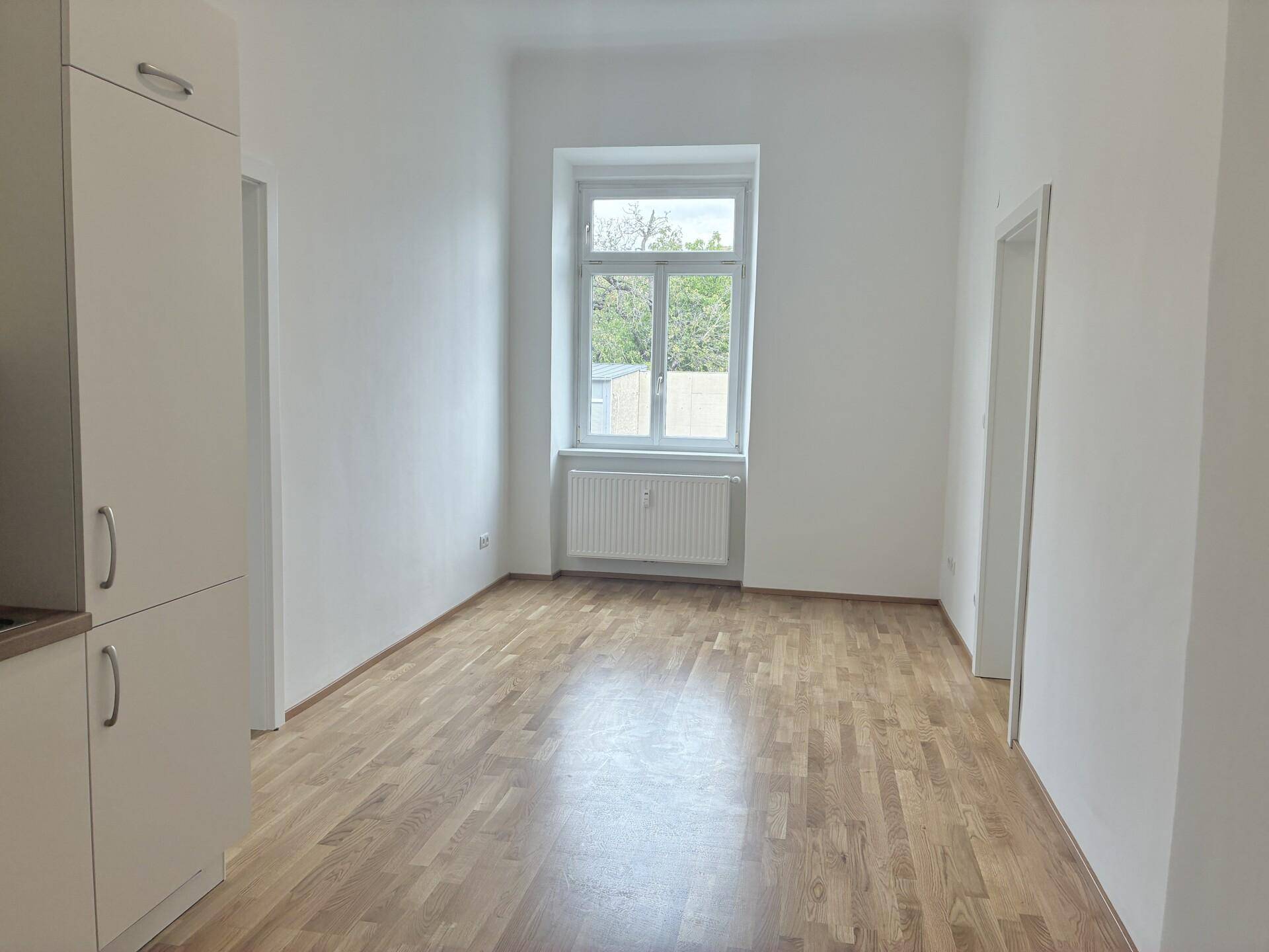 Heller Wohnraum mit Parkettboden, einem großen Fenster und weiß gestrichenen Wänden.