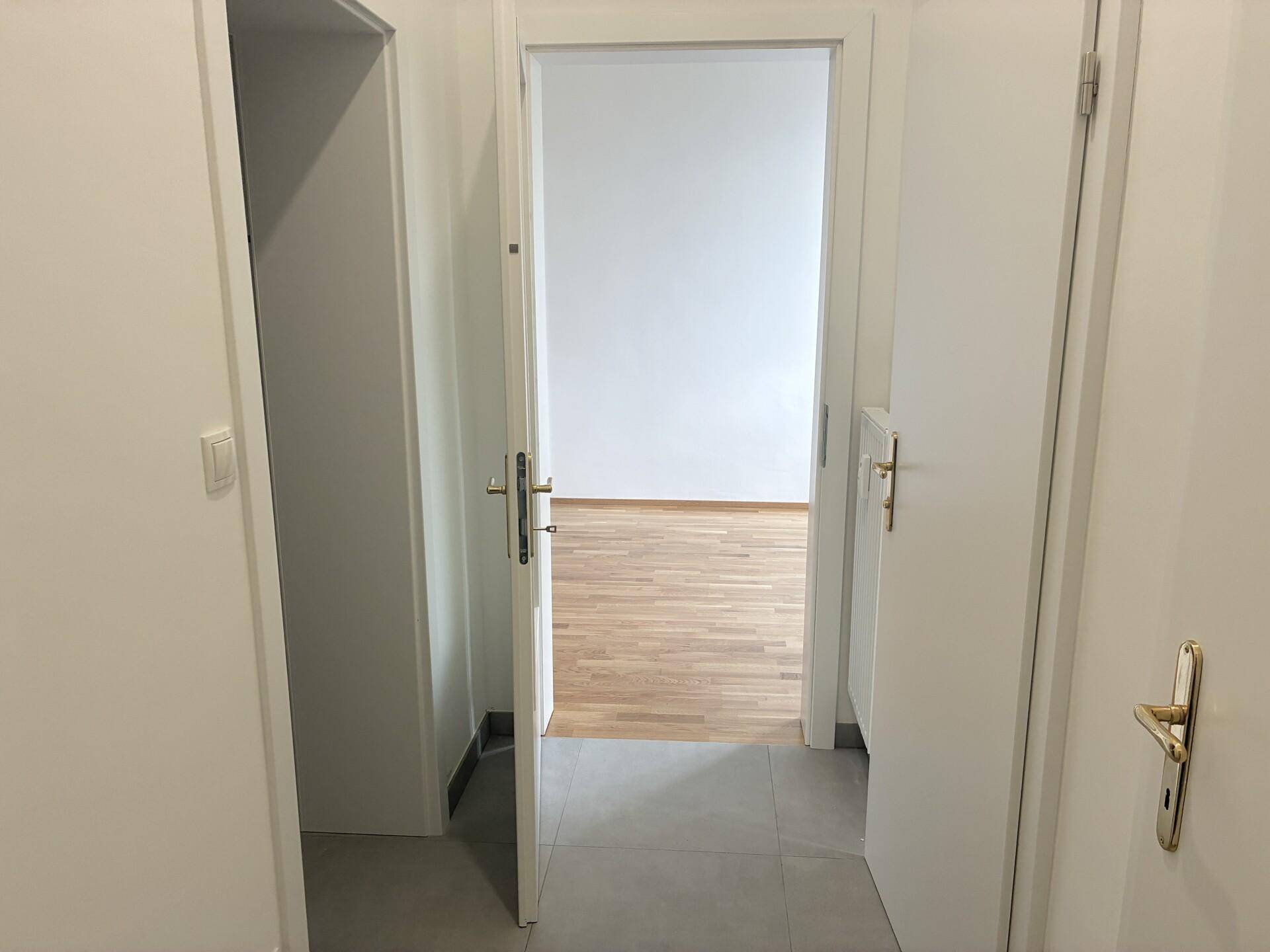 Heller Flur mit grauen Bodenfliesen und Zugang zu verschiedenen Räumen.