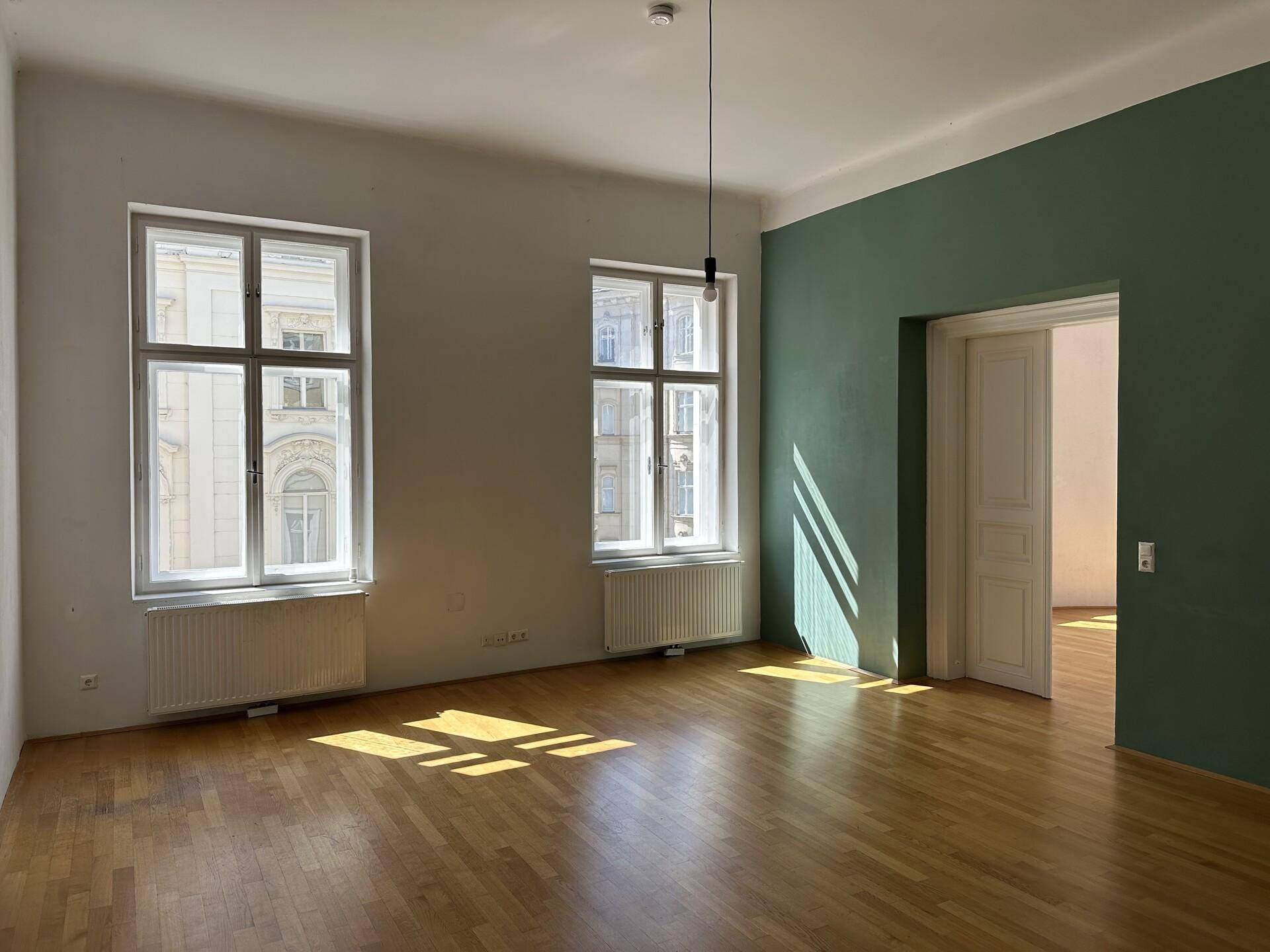 Helles Wohnzimmer mit Parkettboden, hohen Decken und einer grünen Akzentwand.