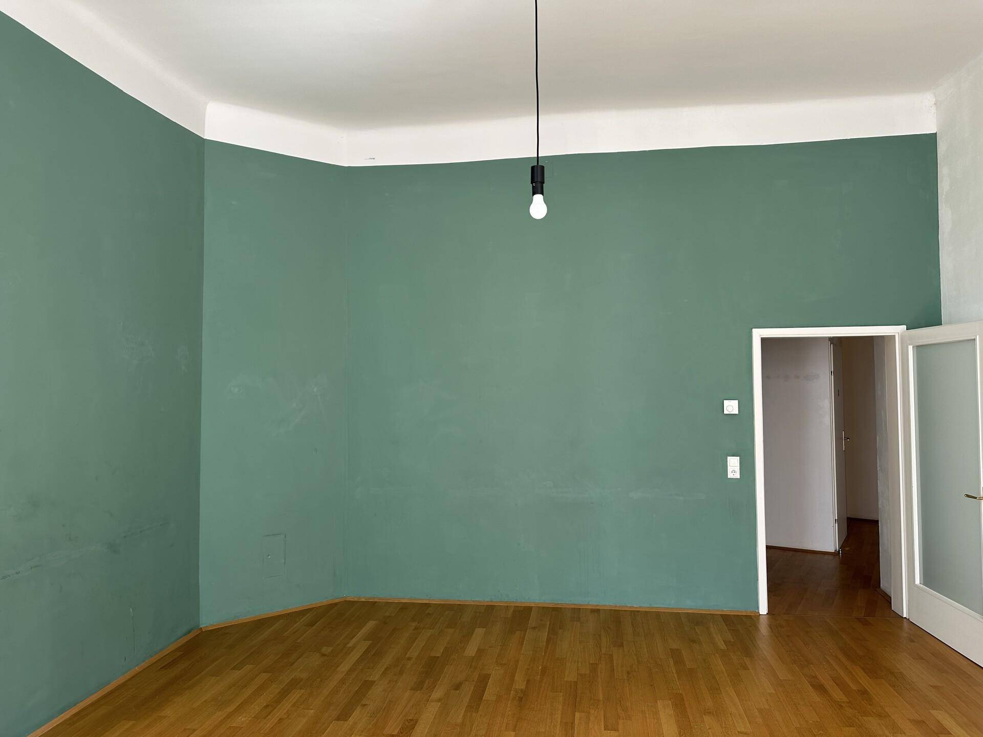 Geräumiges Wohnzimmer mit grüner Wandfarbe und klassischem Parkettboden, bereit zur individuellen Gestaltung.