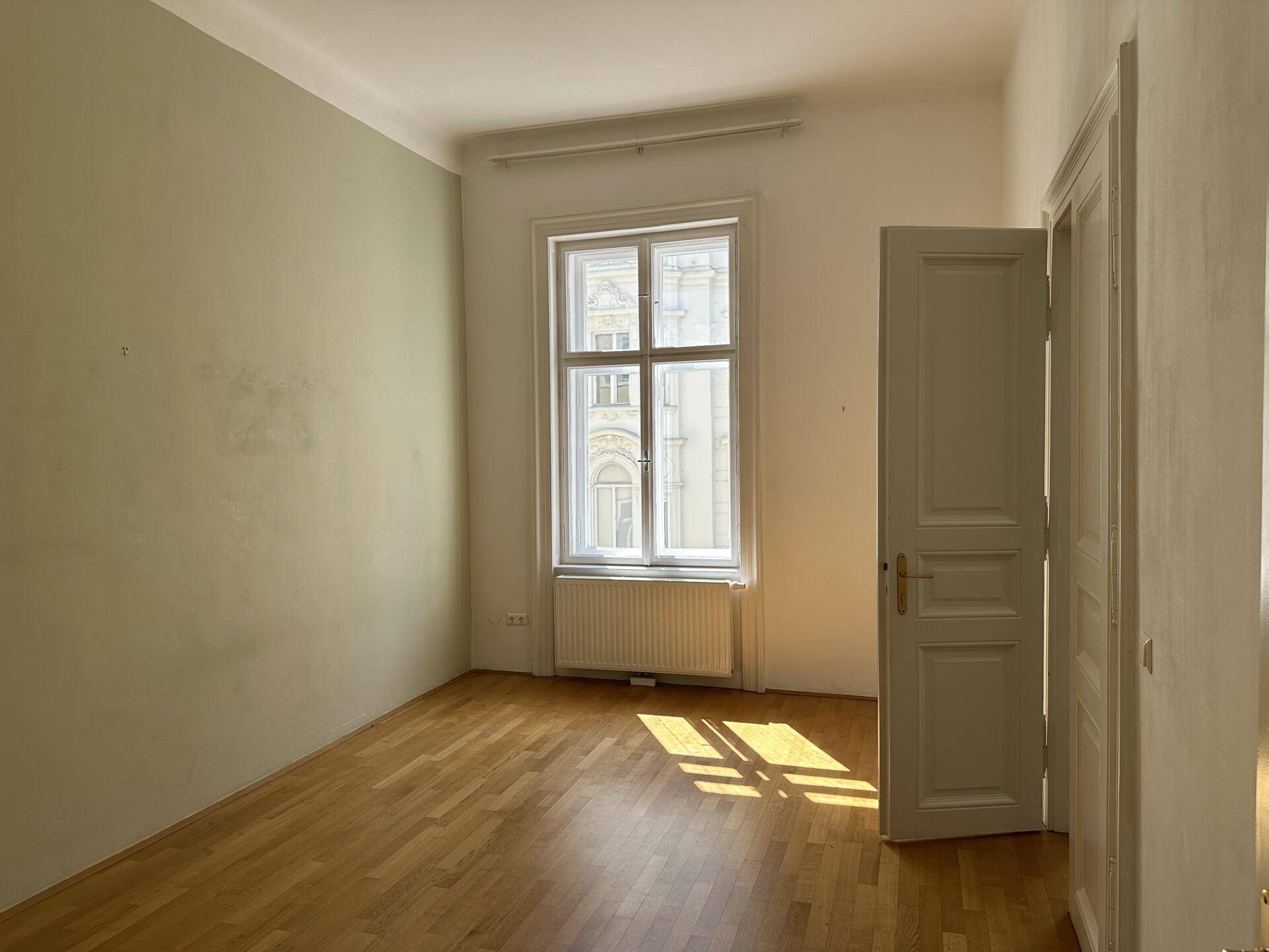 Schlafzimmer mit Parkettboden, einem großen Fenster und heller Wandfarbe, ideal für Ruhe und Entspannung.