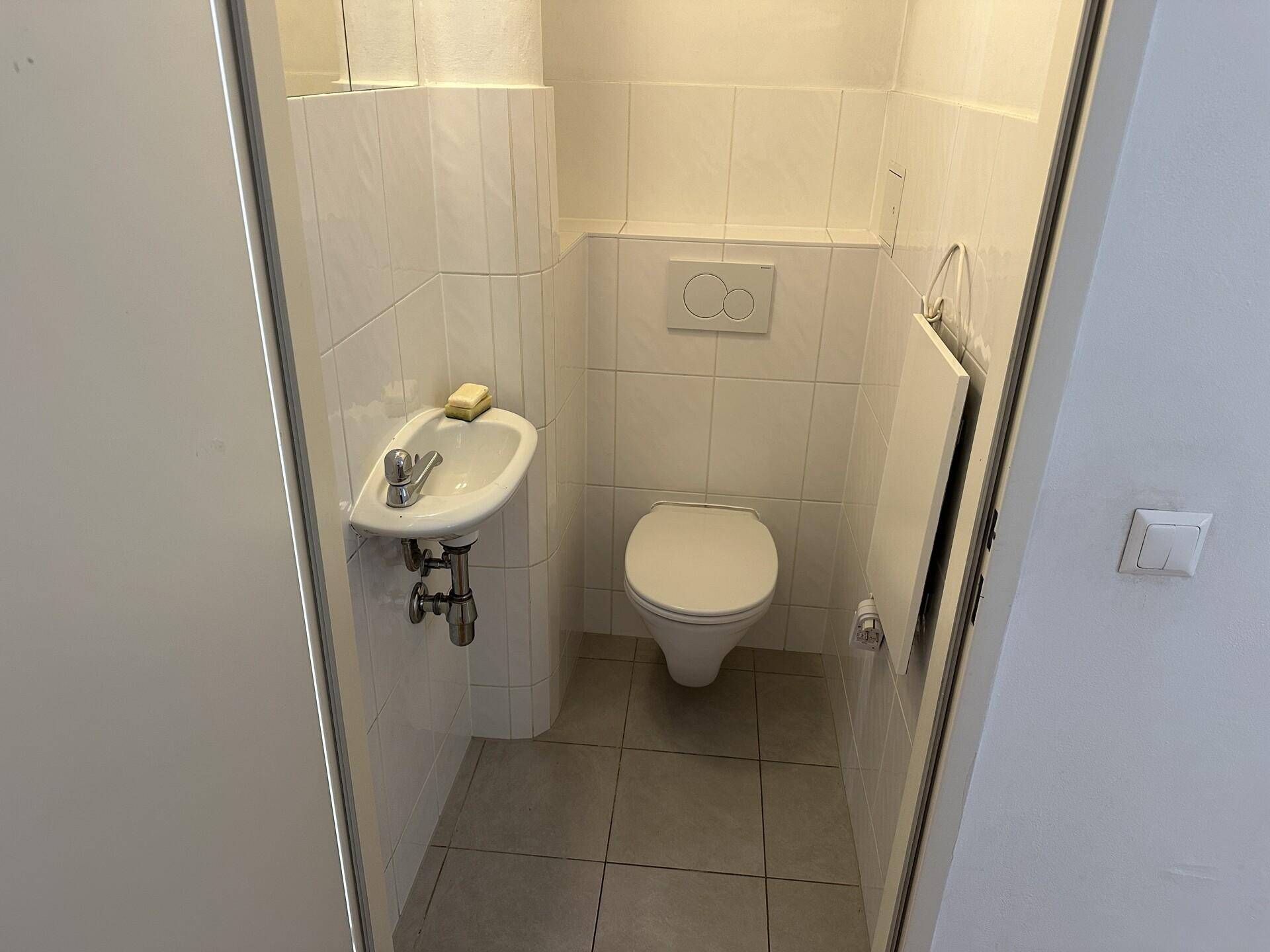 Kleines Gäste-WC mit Wand-WC, Waschbecken und weißen Fliesen, funktional und sauber.