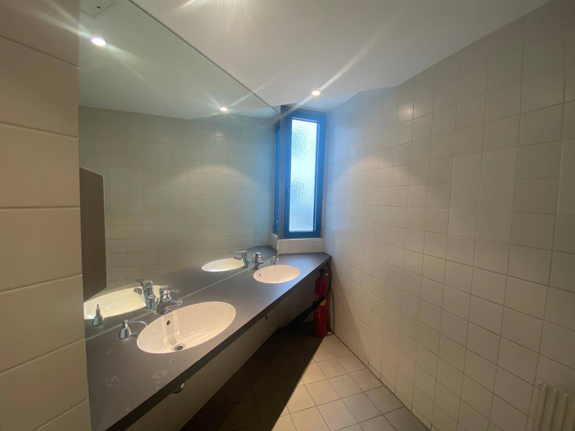 Badezimmer mit zwei Waschbecken, großem Spiegel und einem Fenster, gefliest in hellem Ton.
