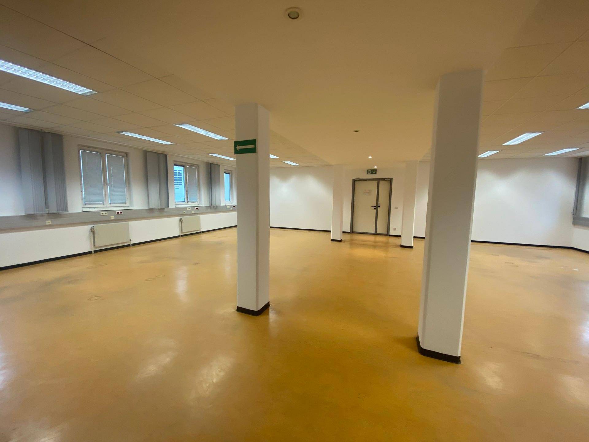 Großer, offener Büroraum mit gelbem Boden, vielen Fenstern und weißen Säulen, bereit zur Einrichtung.