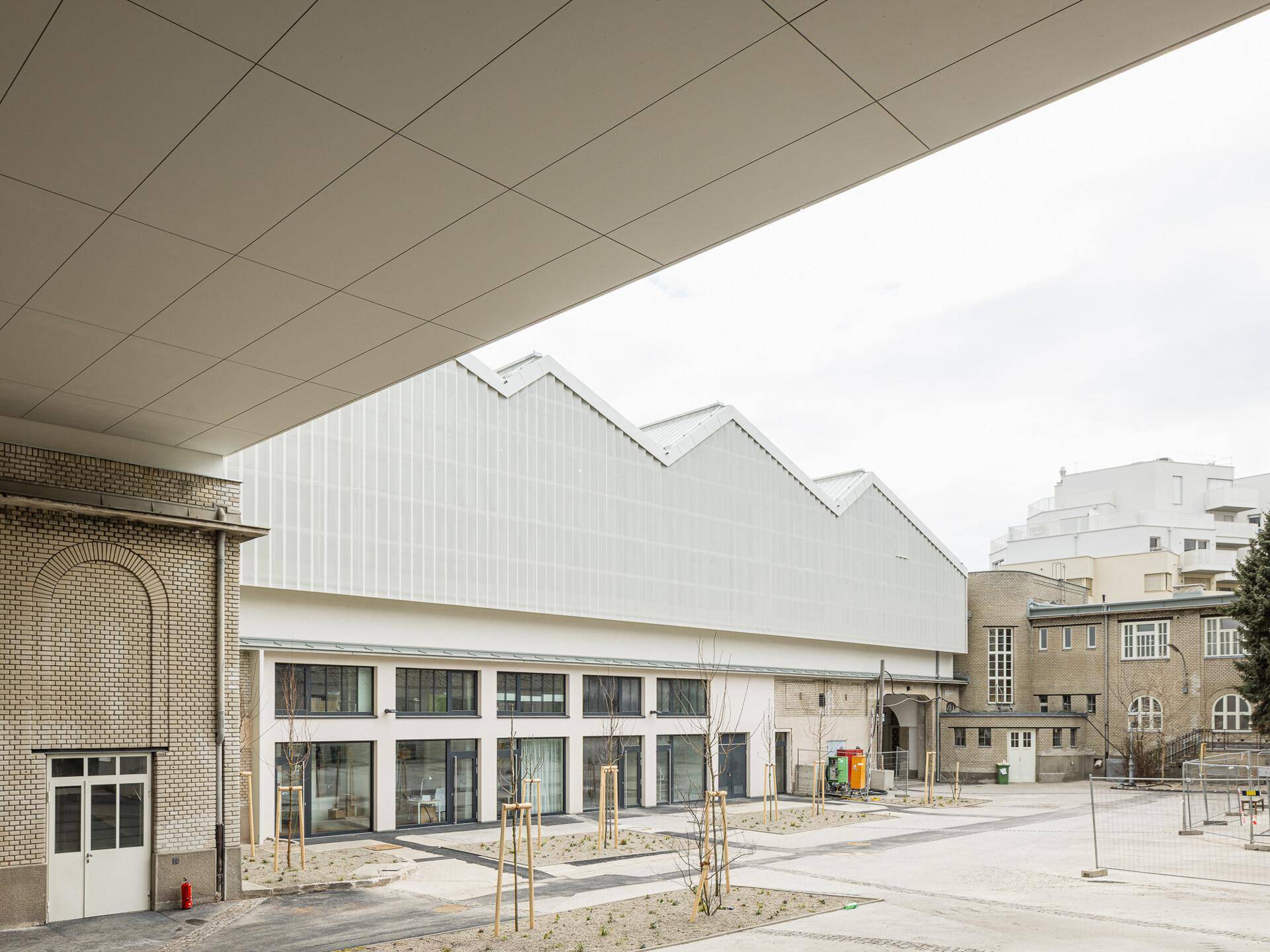 Gebäudekomplex mit einer modernisierten Industriehalle und einer neu gestalteten Außenanlage mit Bäumen.