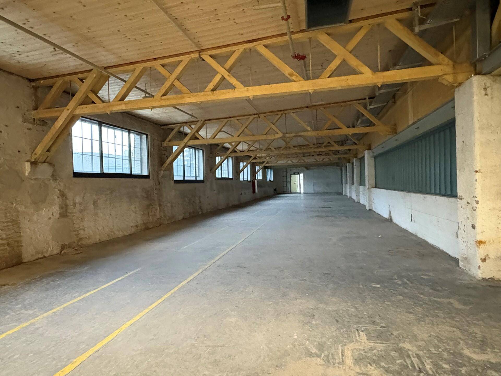 Geräumige Industriehalle mit Holzdachkonstruktion, Betonboden und Reihen von Fenstern für Tageslicht.