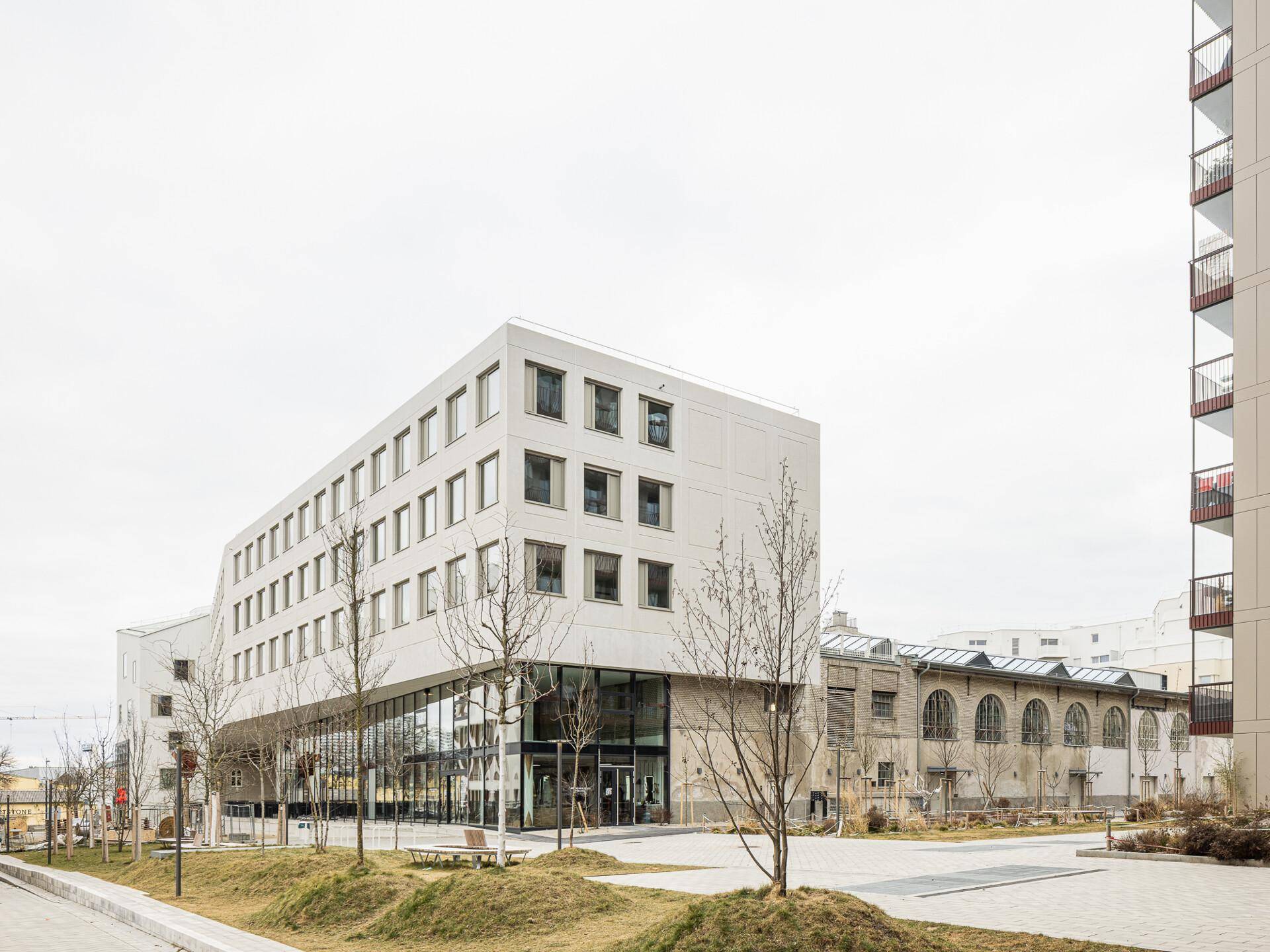 Modernes, weißes Gebäude mit markanter Architektur und großen Glasflächen im Erdgeschoss, eingebettet in eine grüne Umgebung.