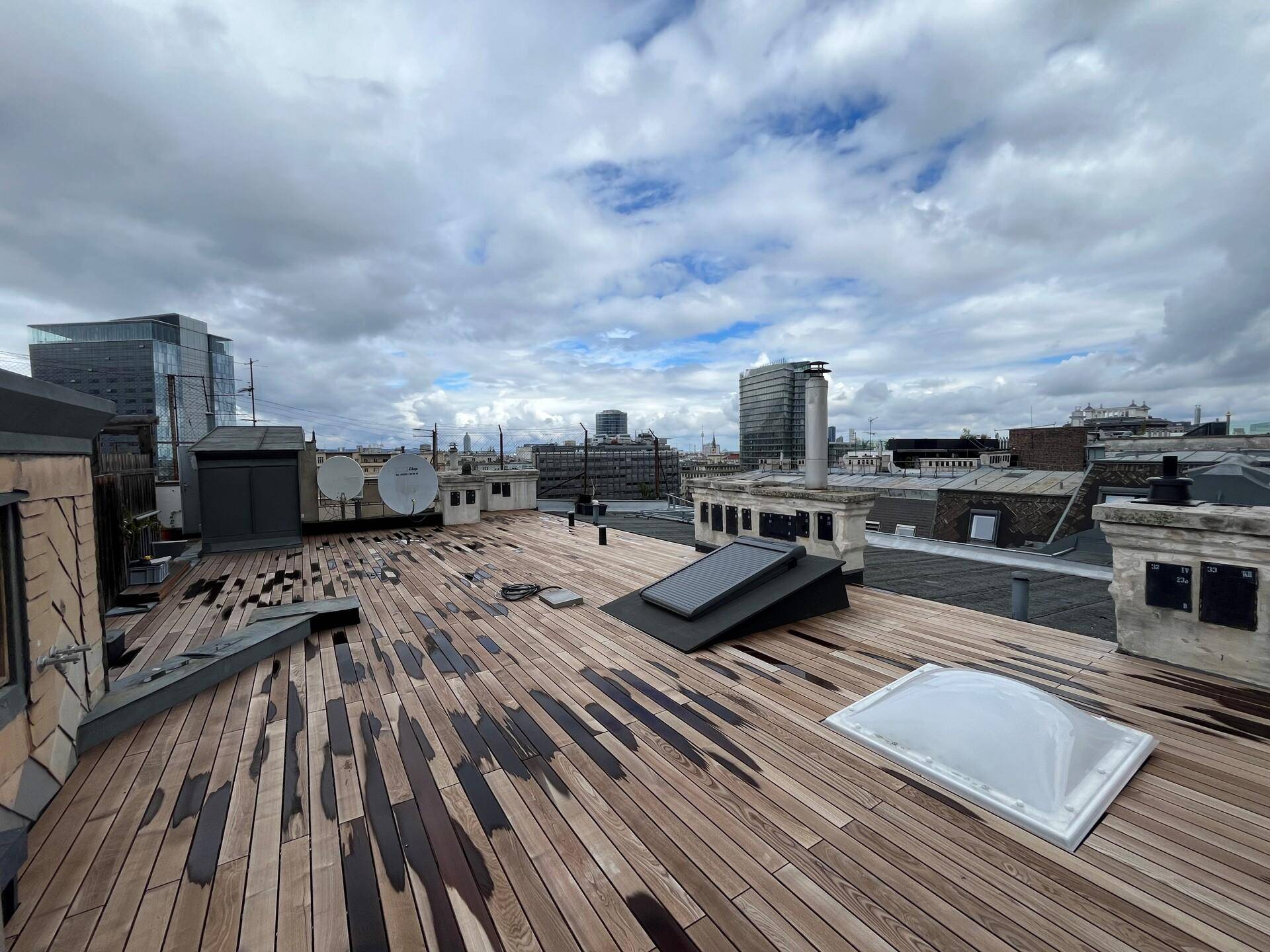 Geräumige Dachterrasse mit Holzbelag und Blick auf die Stadt unter bewölktem Himmel.