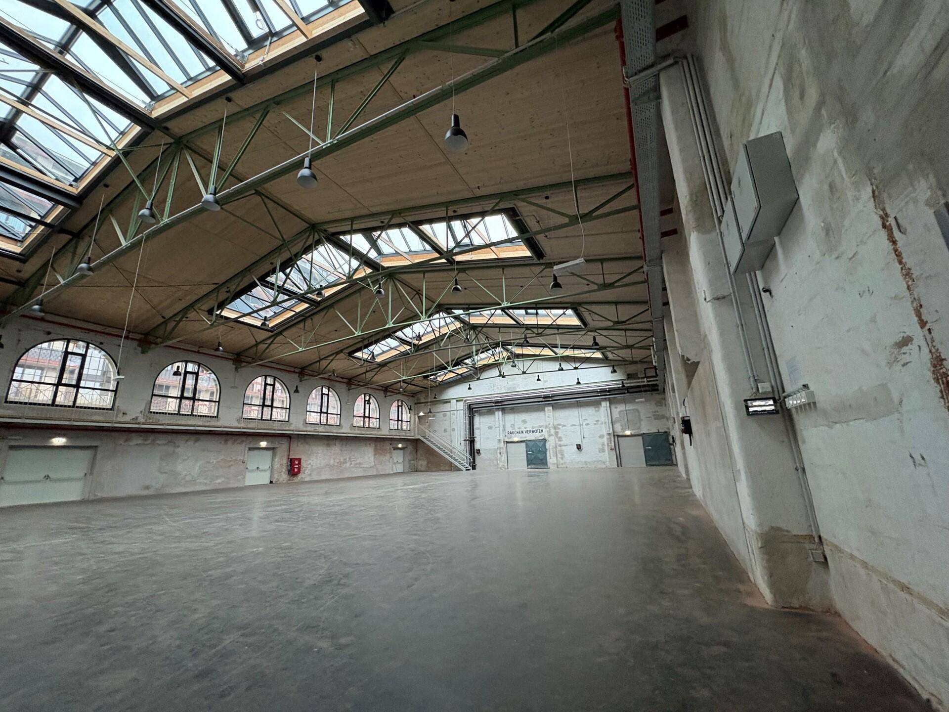 Eine weitläufige Halle mit beeindruckender Dachkonstruktion, vielen Oberlichtern und hohen Wänden.