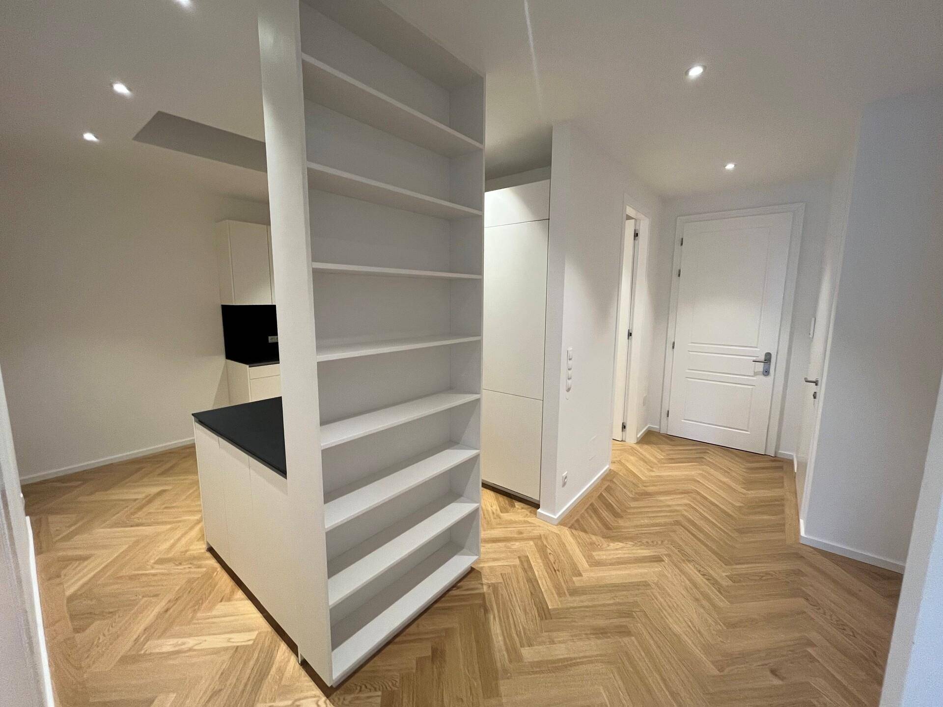 Eingangsbereich mit integriertem Bücherregal und Blick auf die moderne Küche mit Fischgrätparkett.