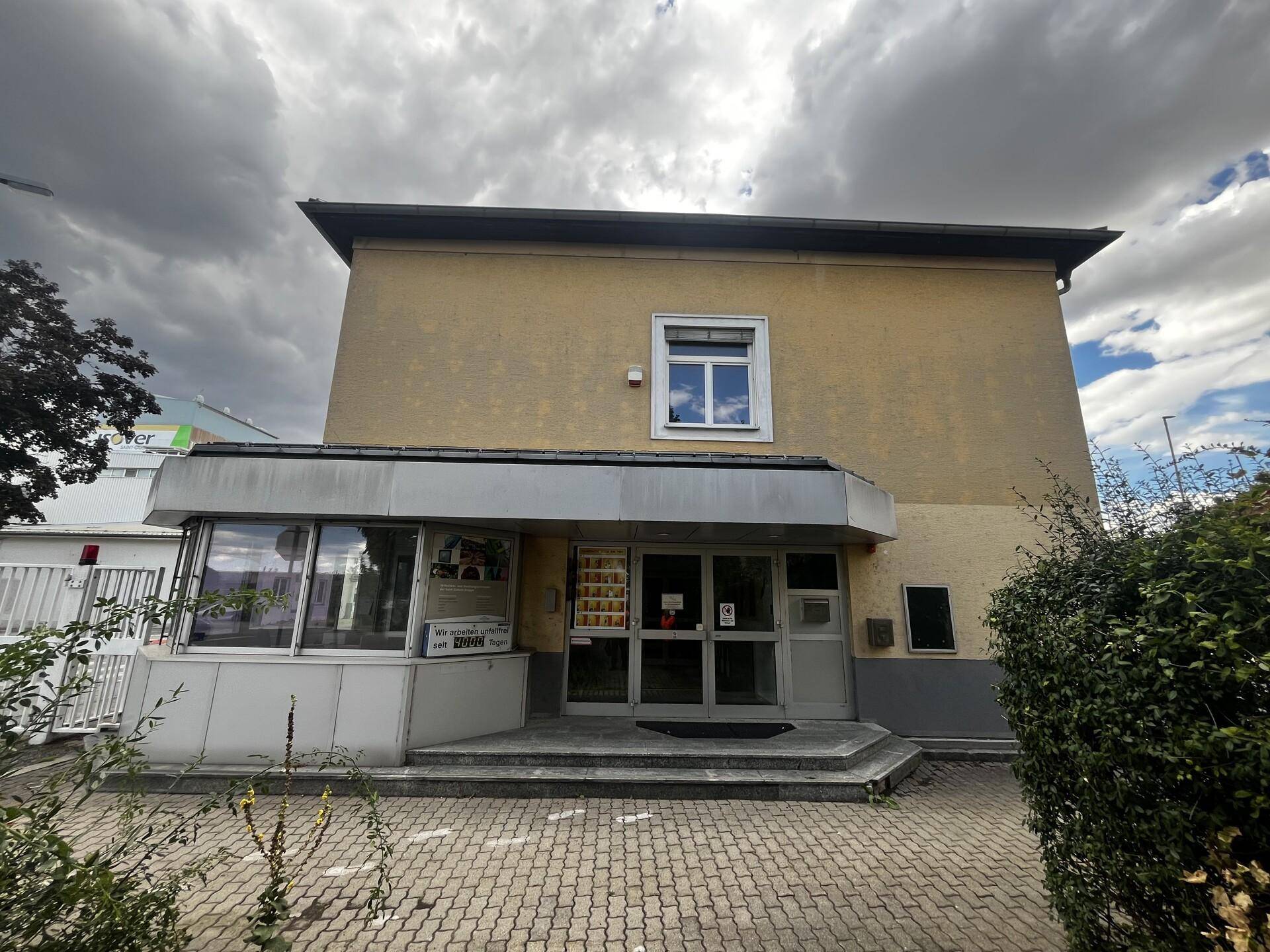 Vorderansicht eines Geschäftsgebäudes mit gelber Fassade, Eingangsbereich und gepflastertem Vorplatz.
