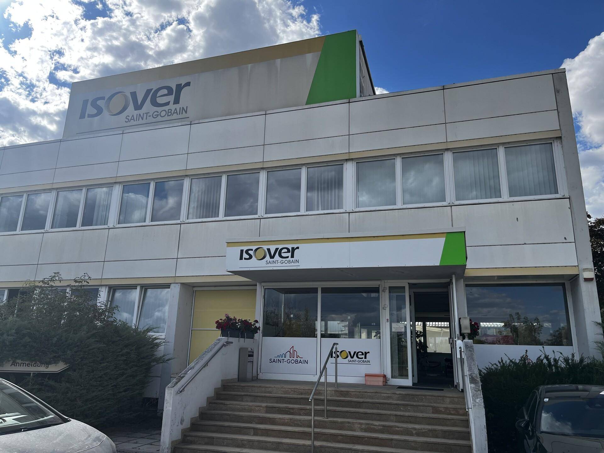 Modernes Bürogebäude mit Glasfassade und ISOVER-Branding, Treppen führen zum Eingangsbereich.