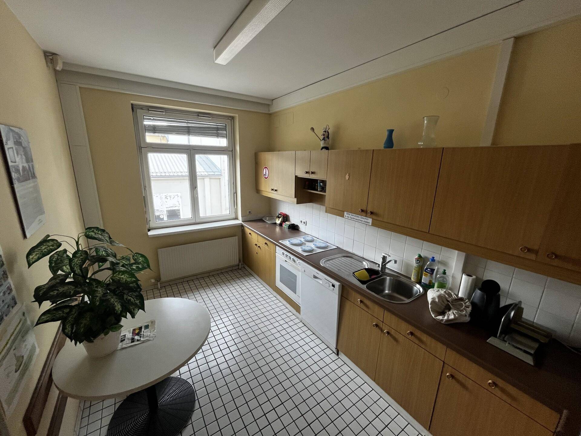 Küche mit Holzschränken, weißem Fliesenspiegel, kariertem Boden und einem Fenster.