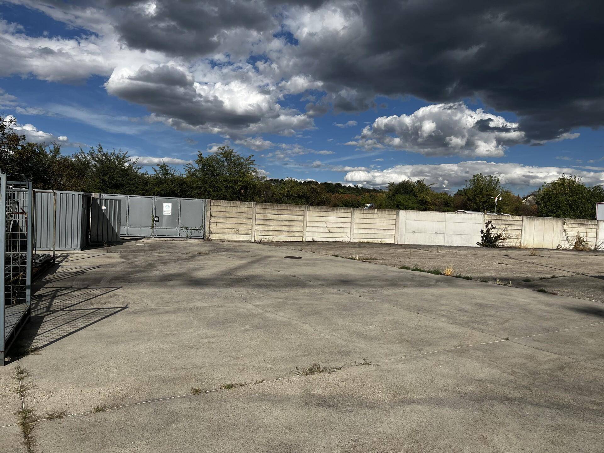 Großer gepflasterter Außenparkplatz, umzäunt von einem Zaun und einer Betonmauer.